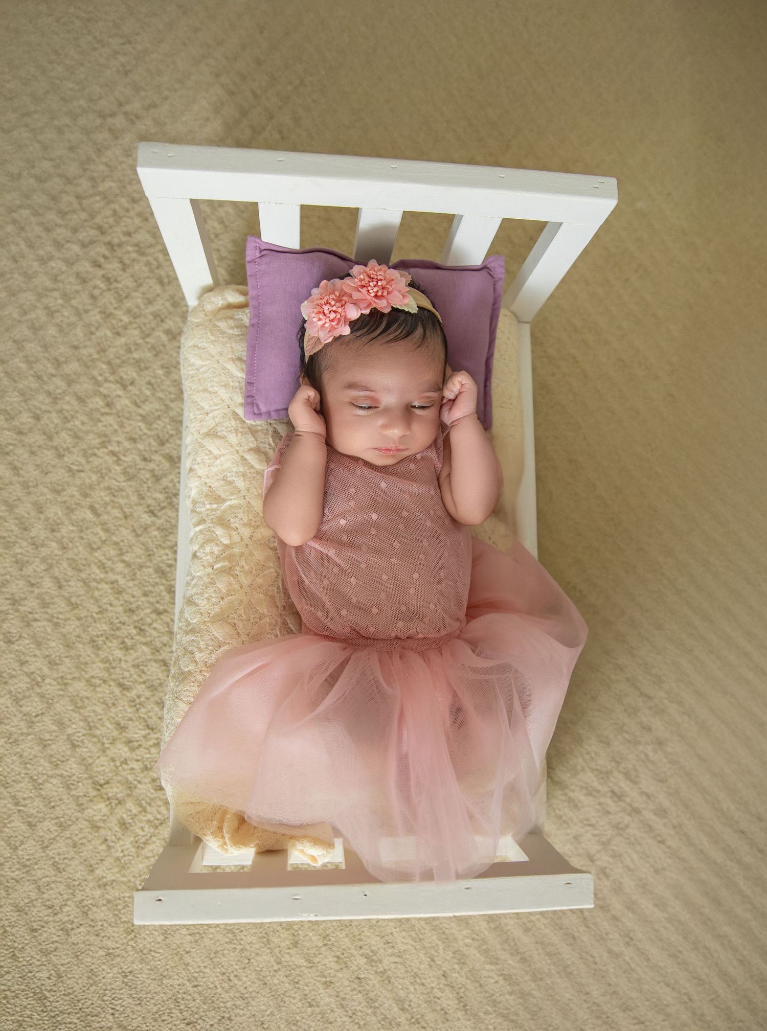 A baby wearing a pink tulle dress lies on beige carpet in three similar poses.