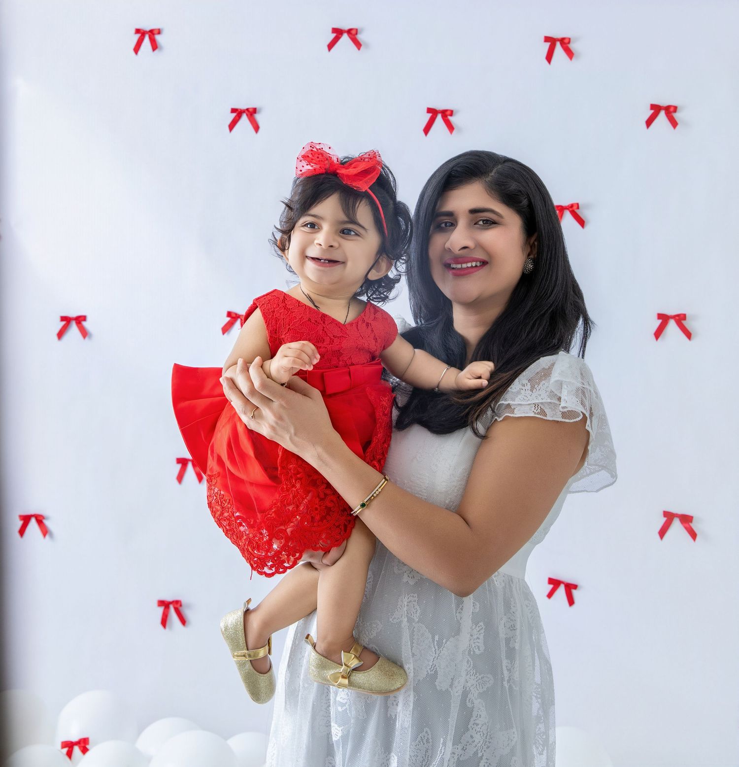 Adult and child in festive red and white outfits pose against decorated background.
