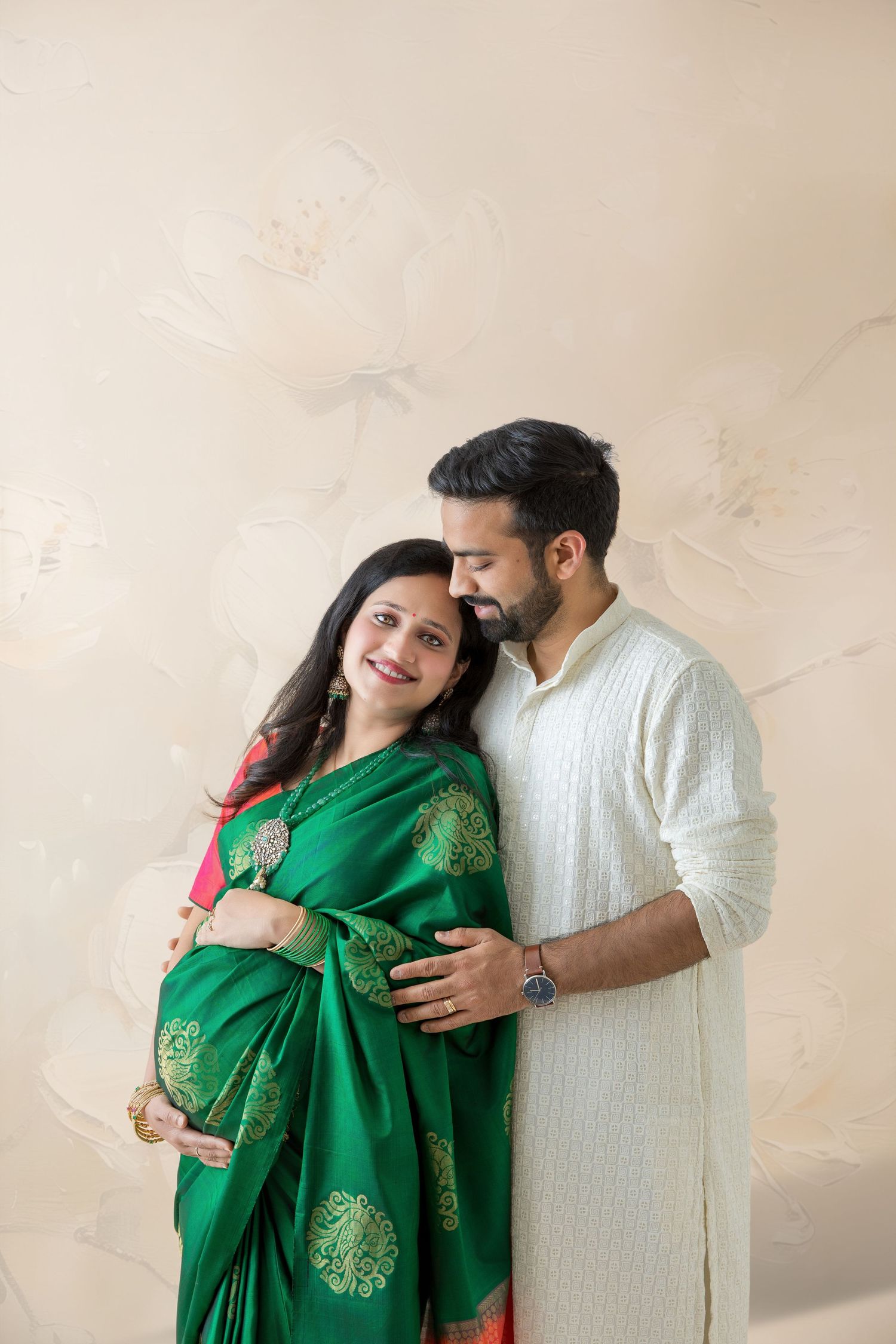 Pregnant Indian woman in green saree with husband in white kurta posing together for maternity photoshoot.