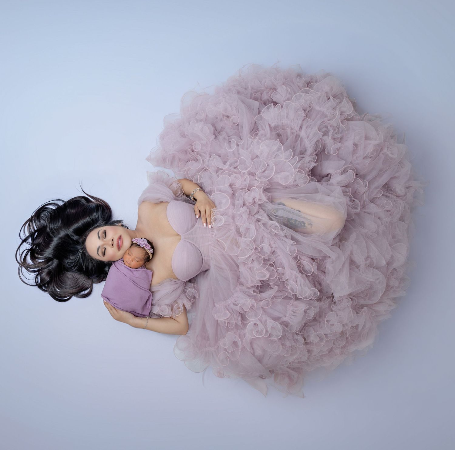 Woman in a voluminous dusty pink ruffled tulle maternity gown lying gracefully on a white studio floor.