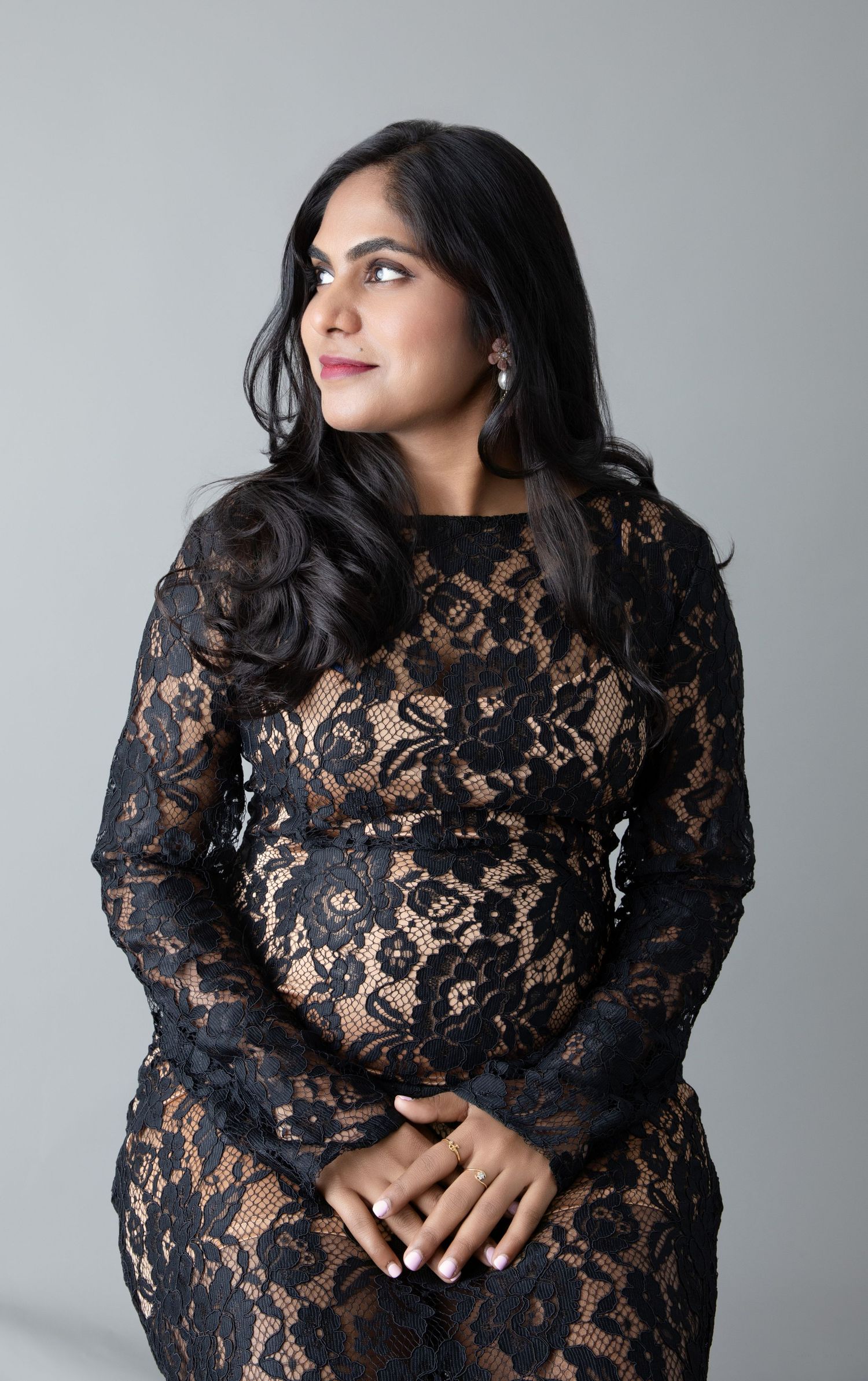Side profile studio portrait of woman in black lace dress looking to the left.