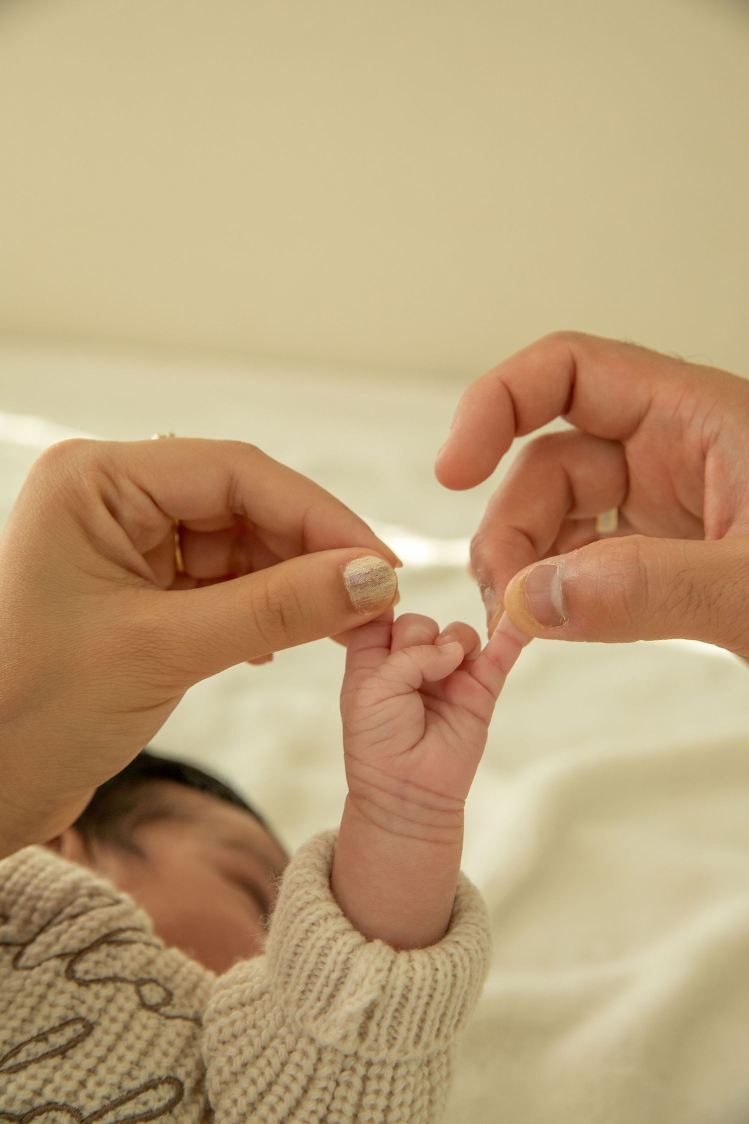 A series of hands holding and gently touching a baby's tiny fingers against a soft cream-colored background.