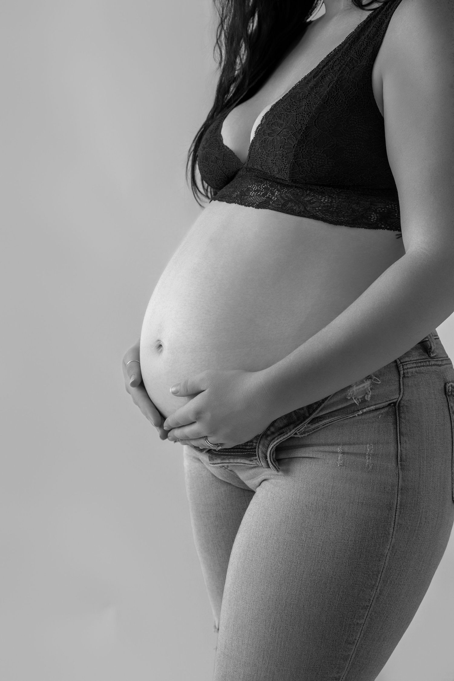Black and white photo series showing progression of pregnancy belly growth while wearing jeans and dark top.