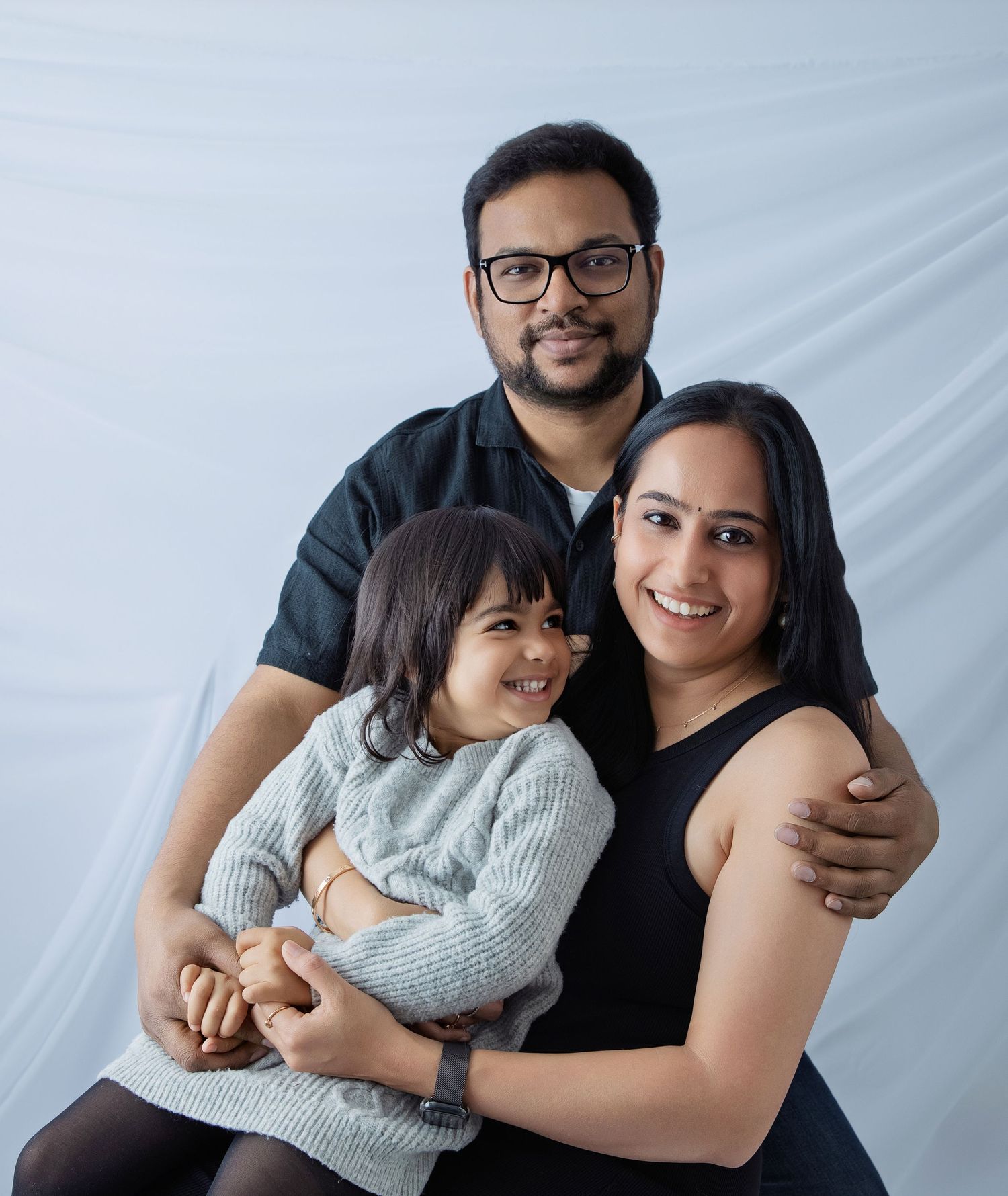 A family poses together in matching black and white outfits against a light blue studio backdrop.
