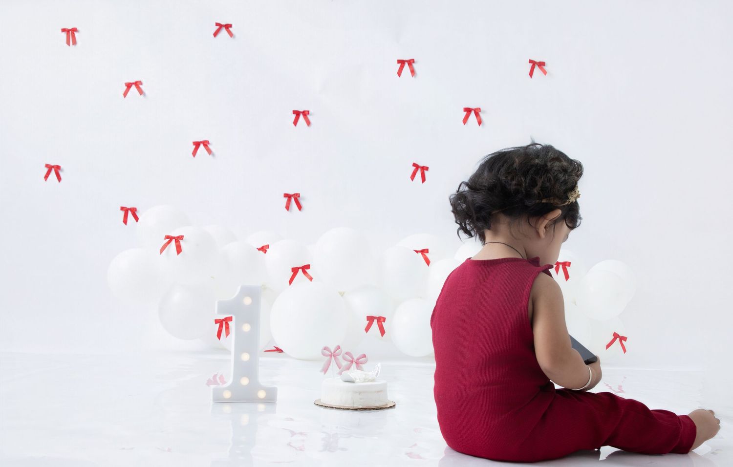 A child in a burgundy shirt sits on a white floor with red decorative elements scattered around.