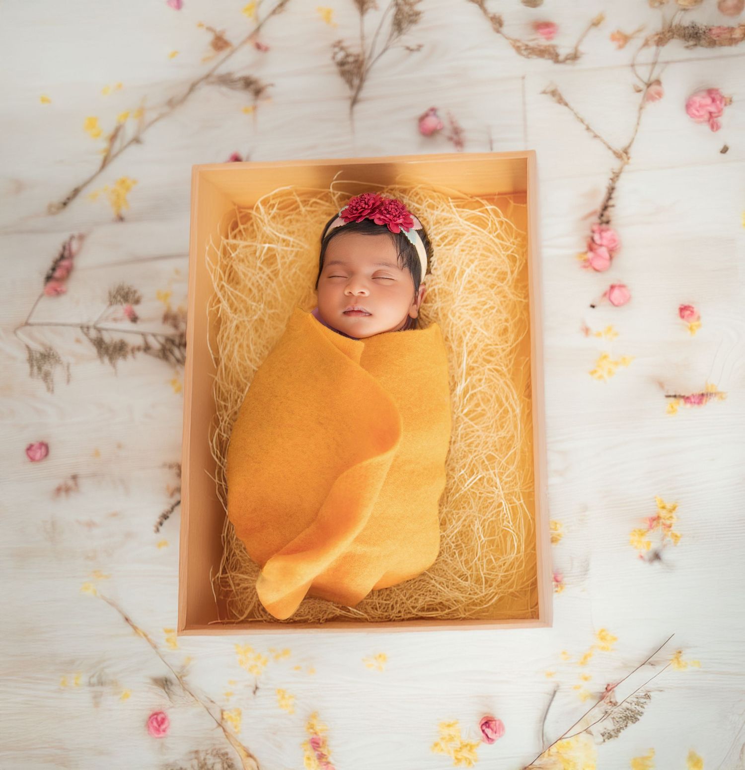 A newborn baby rests peacefully on an orange blanket surrounded by delicate floral patterns.