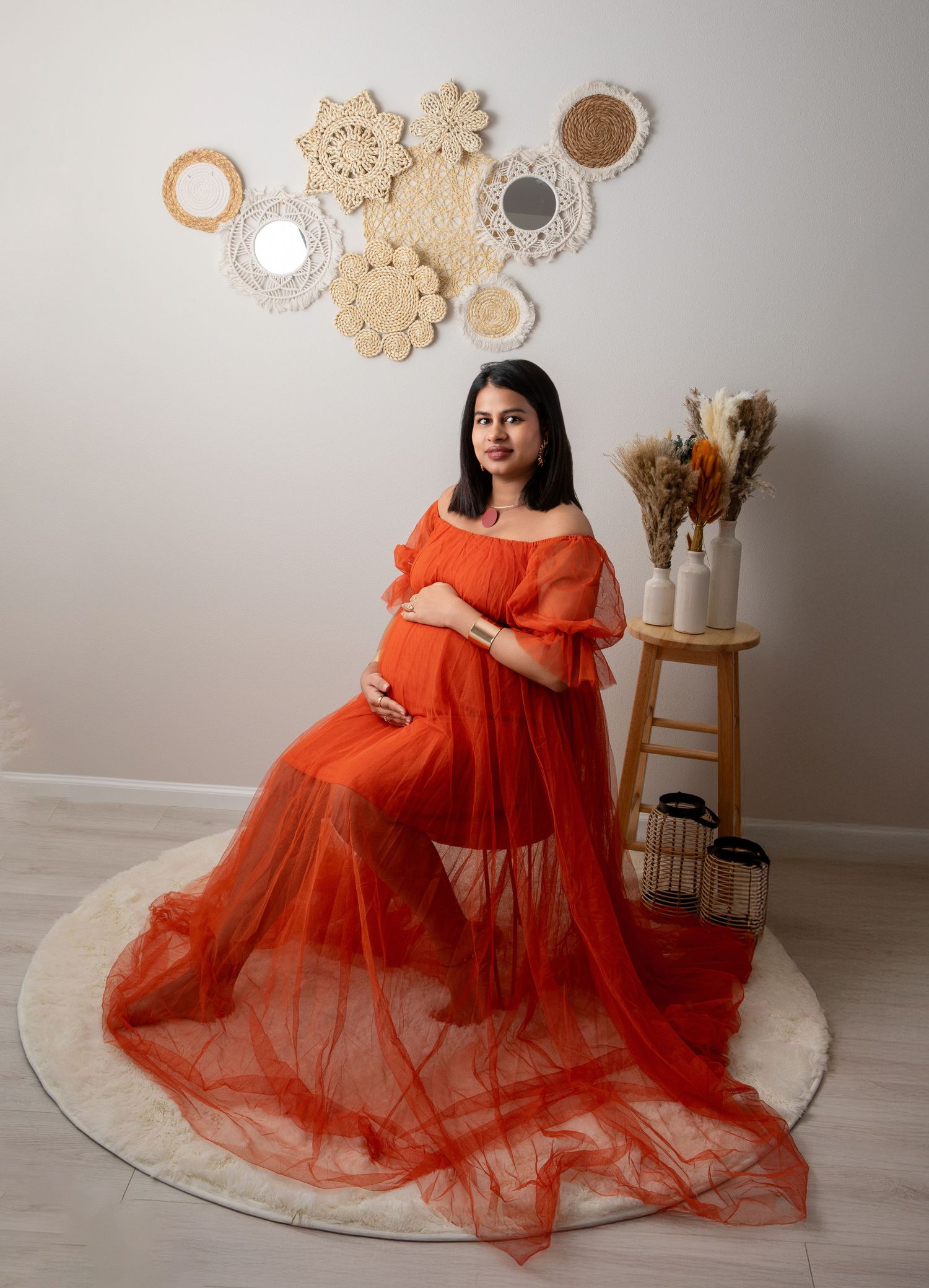 A person in a flowing orange tulle dress poses elegantly against a light backdrop with decorative wall hangings.