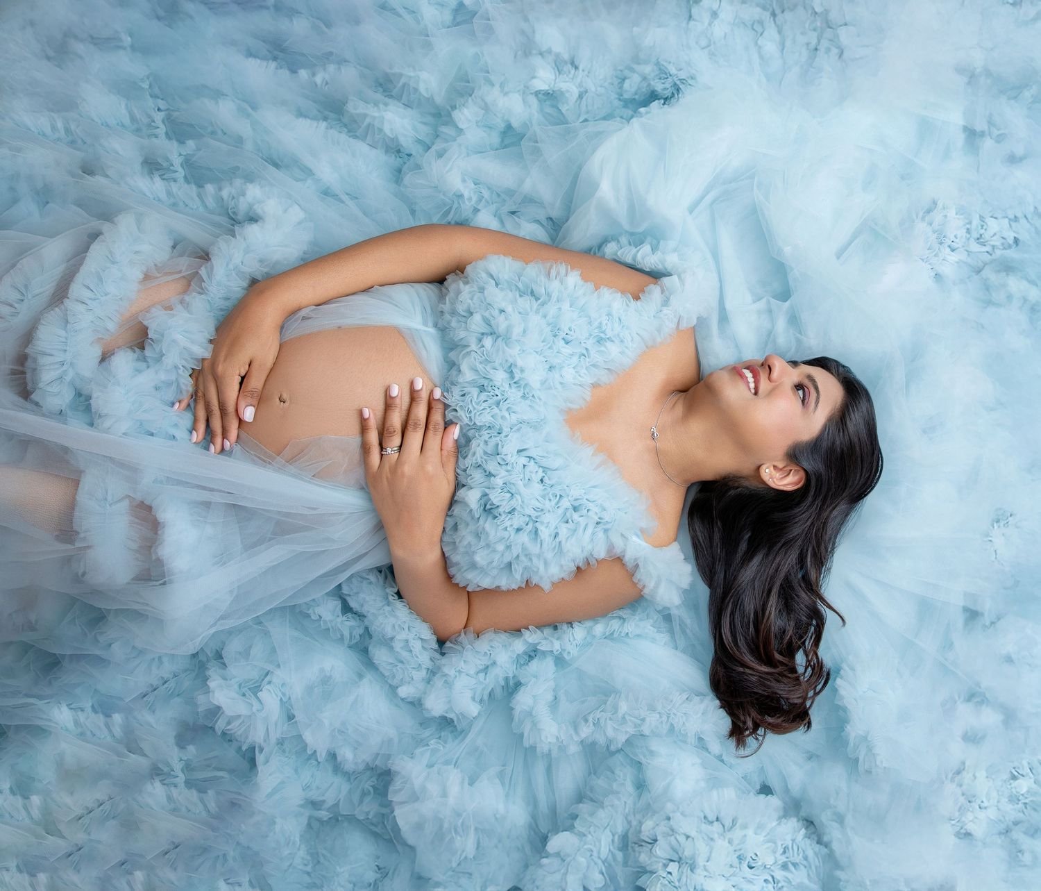 Ethereal maternity photos with flowing blue tulle dress against light background.