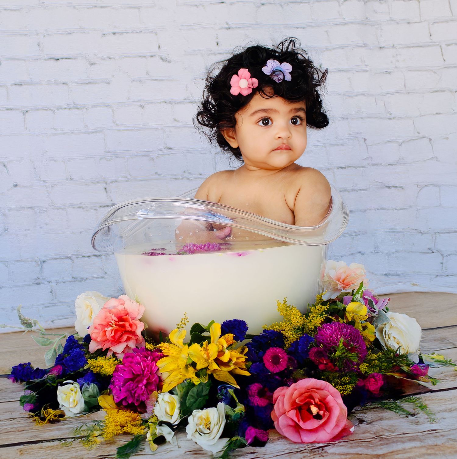 Baby bath photography with colorful floral arrangements around white tub.