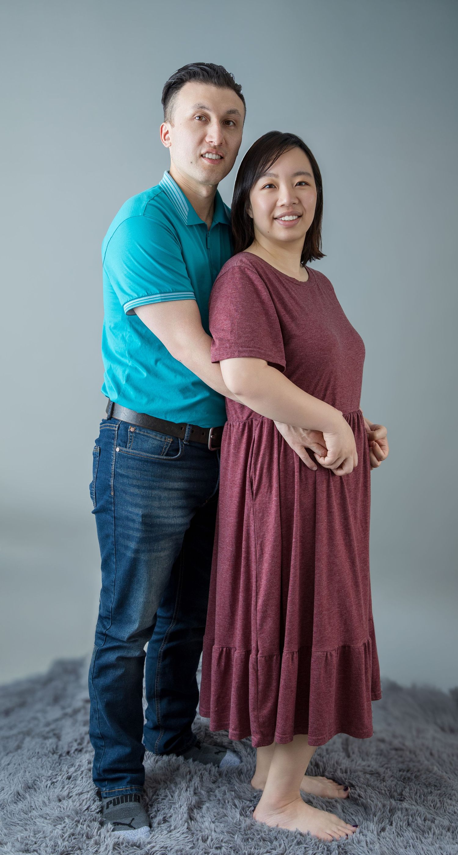 Couple embracing in casual outfits against studio background.