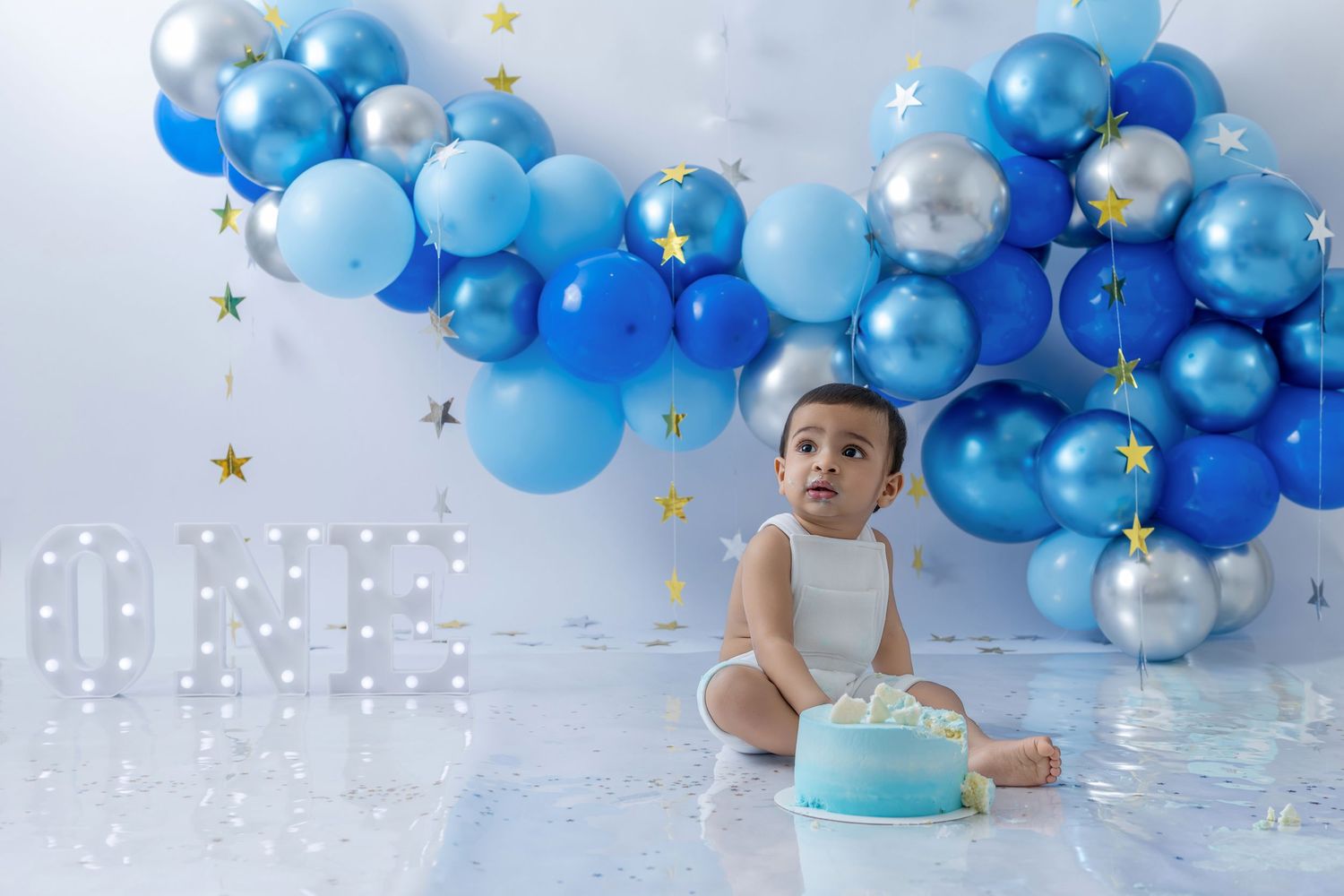 Blue and silver balloon garland decorates a first birthday cake smash photo session with festive stars and decor.
