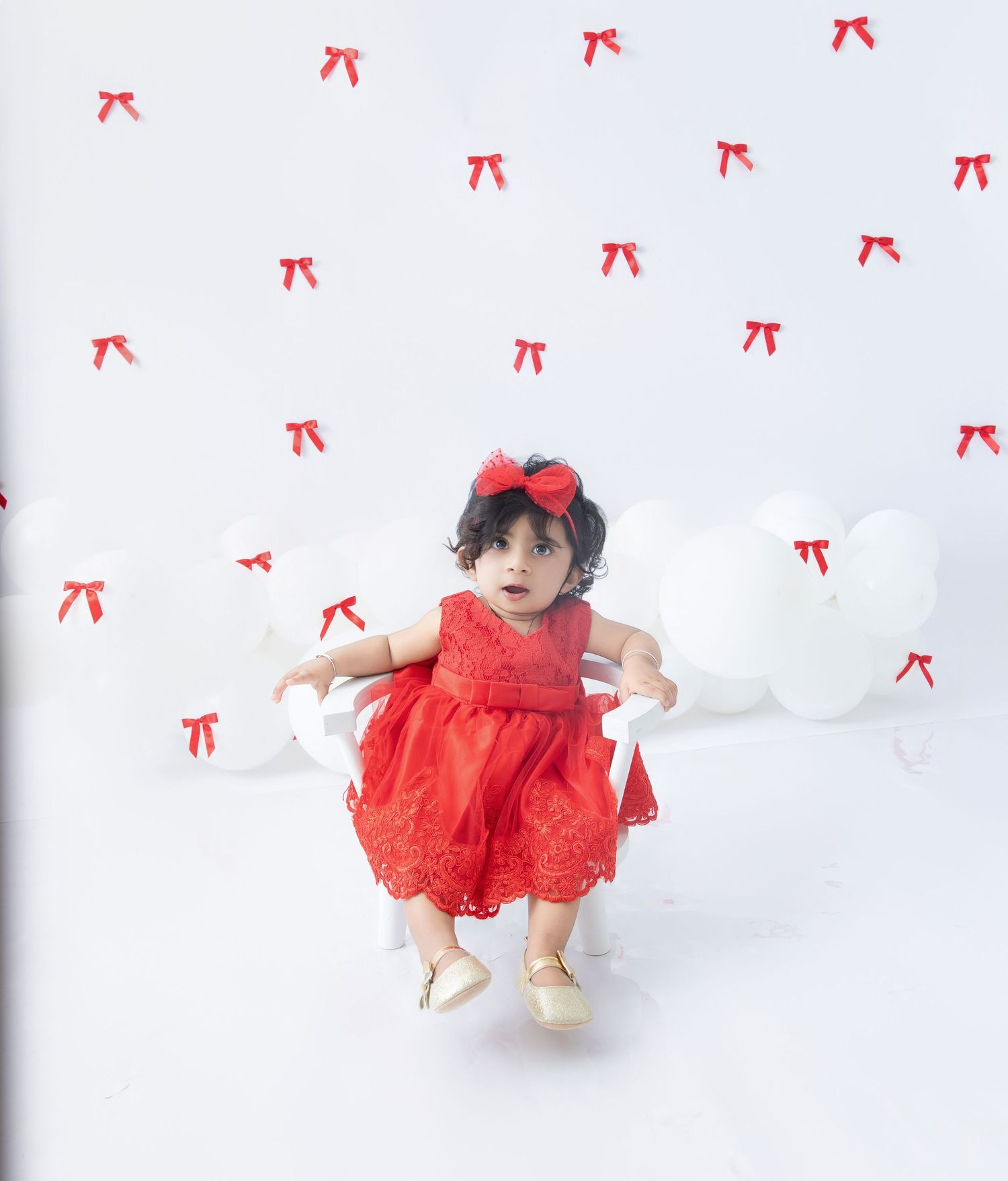 Small child in red dress twirls and plays on white floor with red bow decorations.