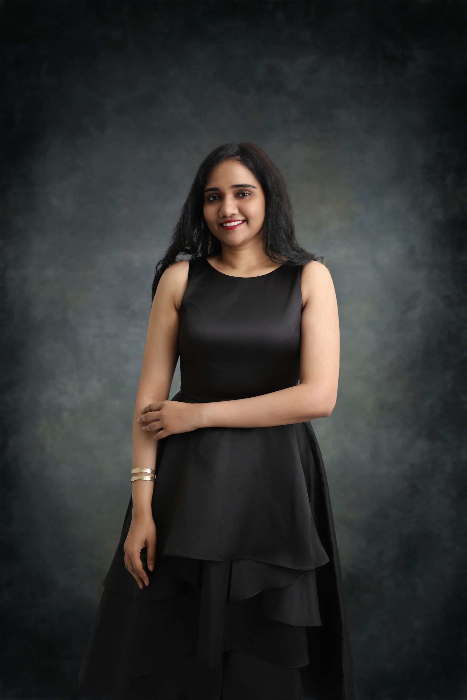 An elegant black layered dress is showcased against a moody dark backdrop in this professional portrait.