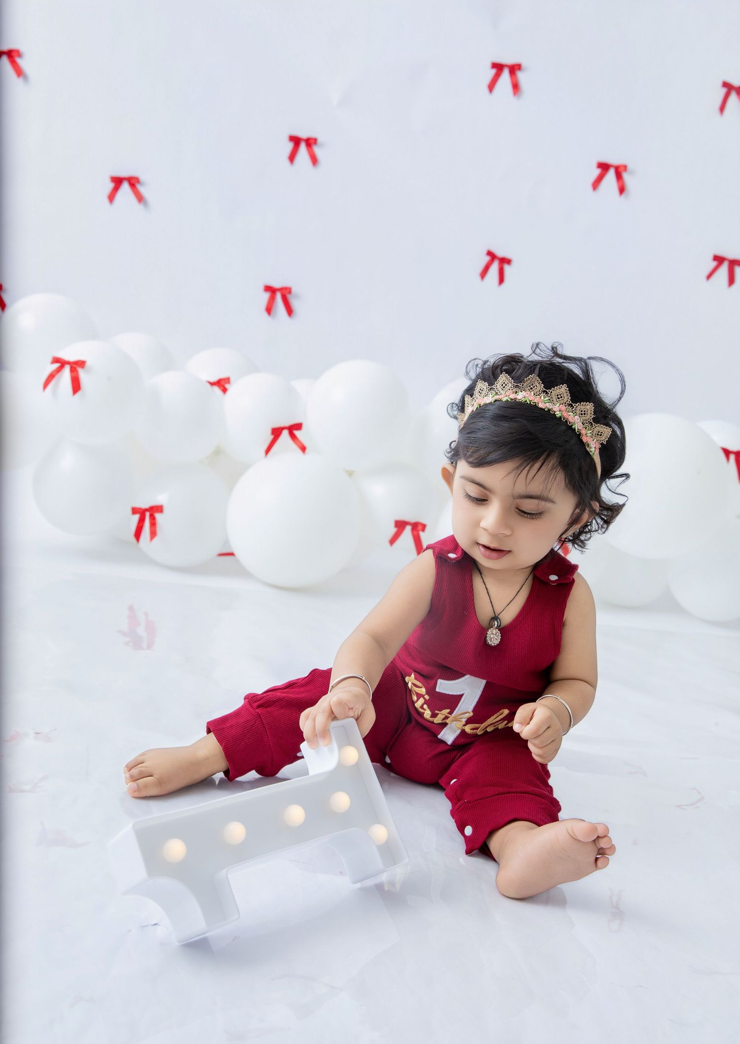 Toddler in red outfit plays with illuminated number one against white backdrop.