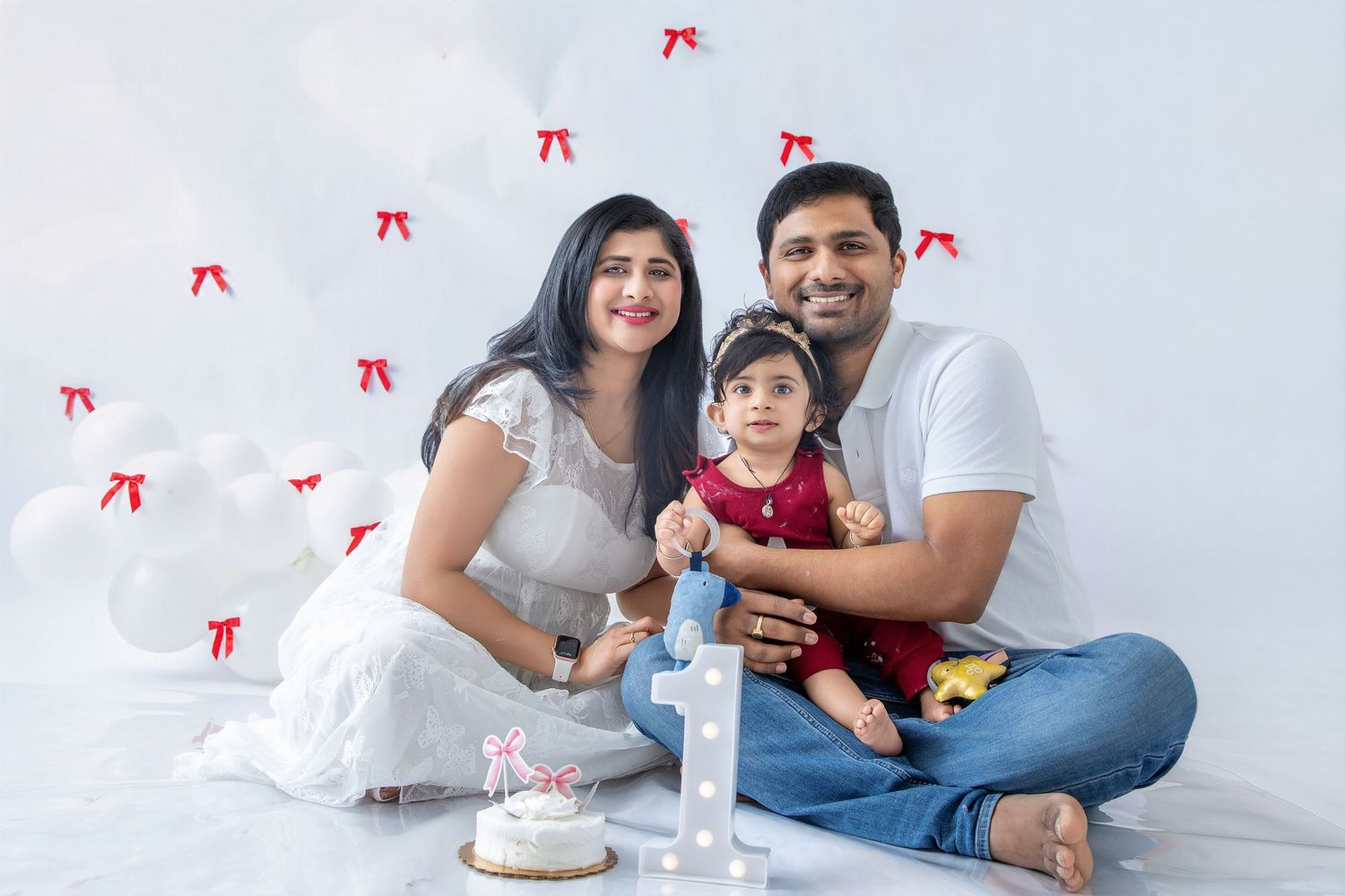 A family sits together on a white floor with red decorative elements during a celebration.