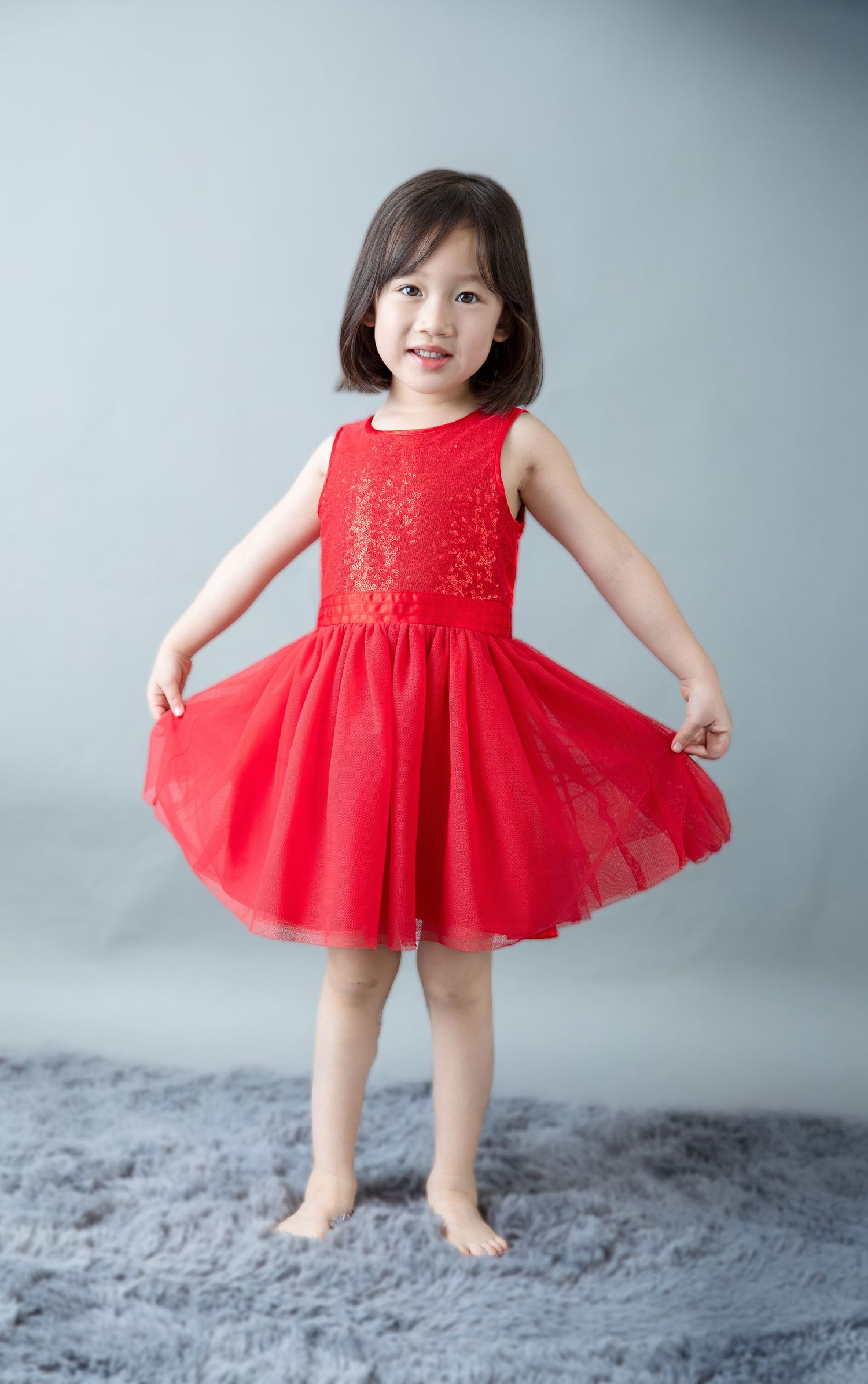 Young child wearing a bright red tulle party dress twirls and dances on a gray studio background.