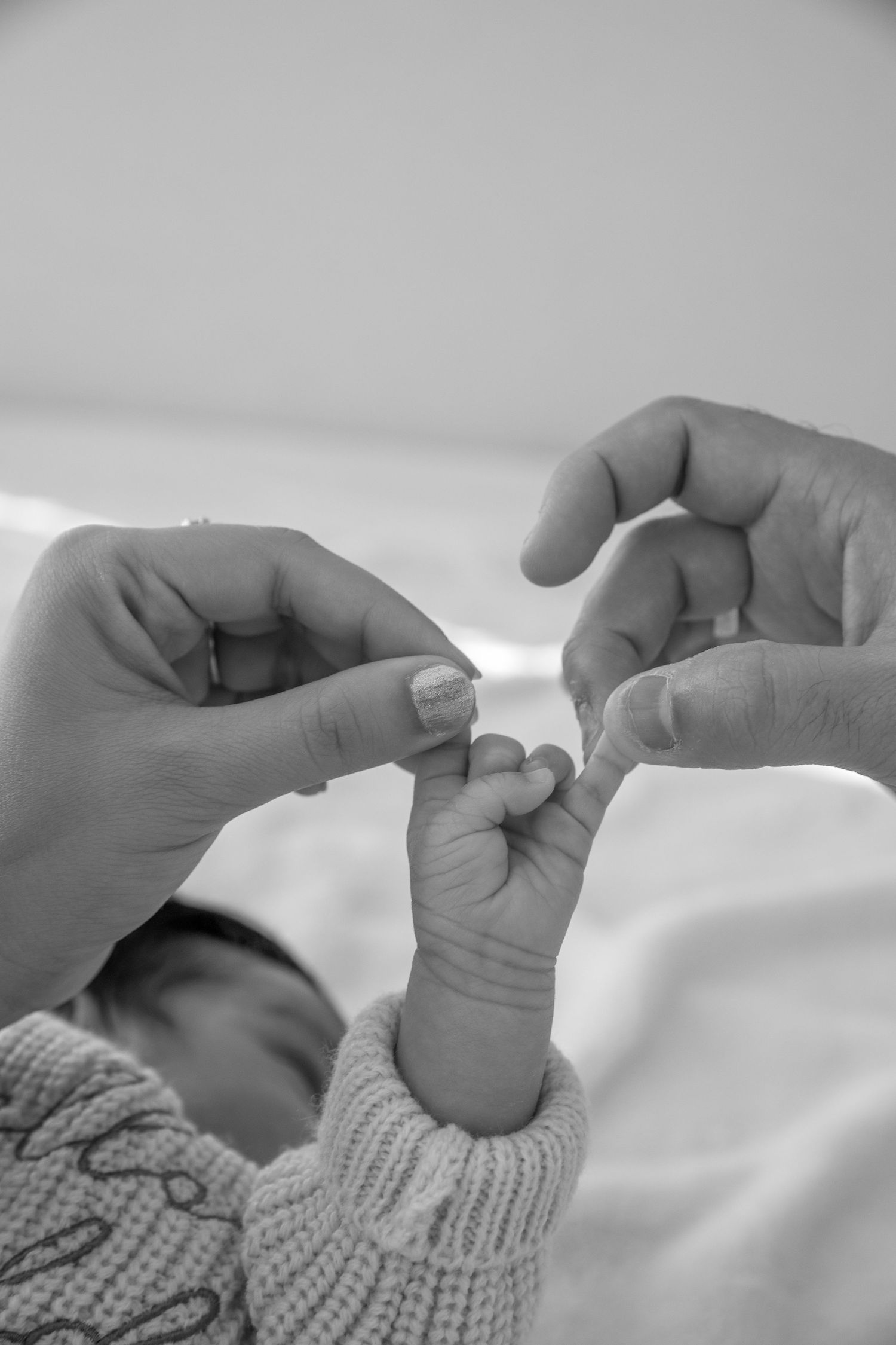 Adult hands gently hold a tiny baby foot wearing a knitted sweater in black and white.