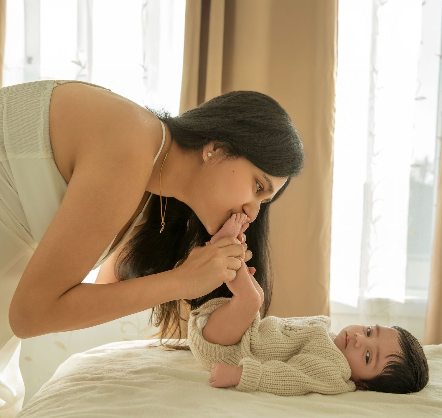 Mother and baby share a tender bonding moment in a sunlit bedroom.