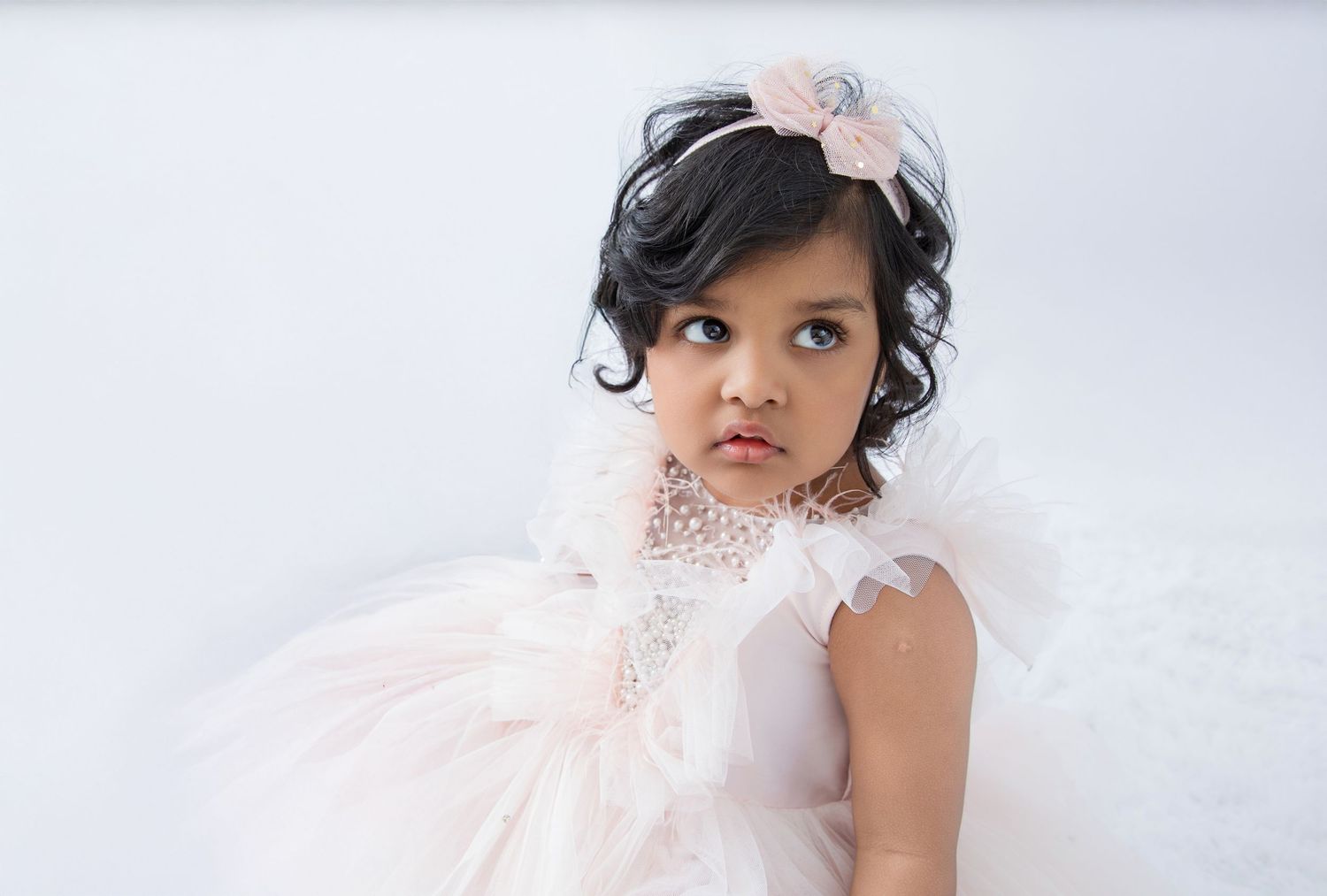 Child wearing pink tulle dress and hair accessory in dreamy studio portrait.
