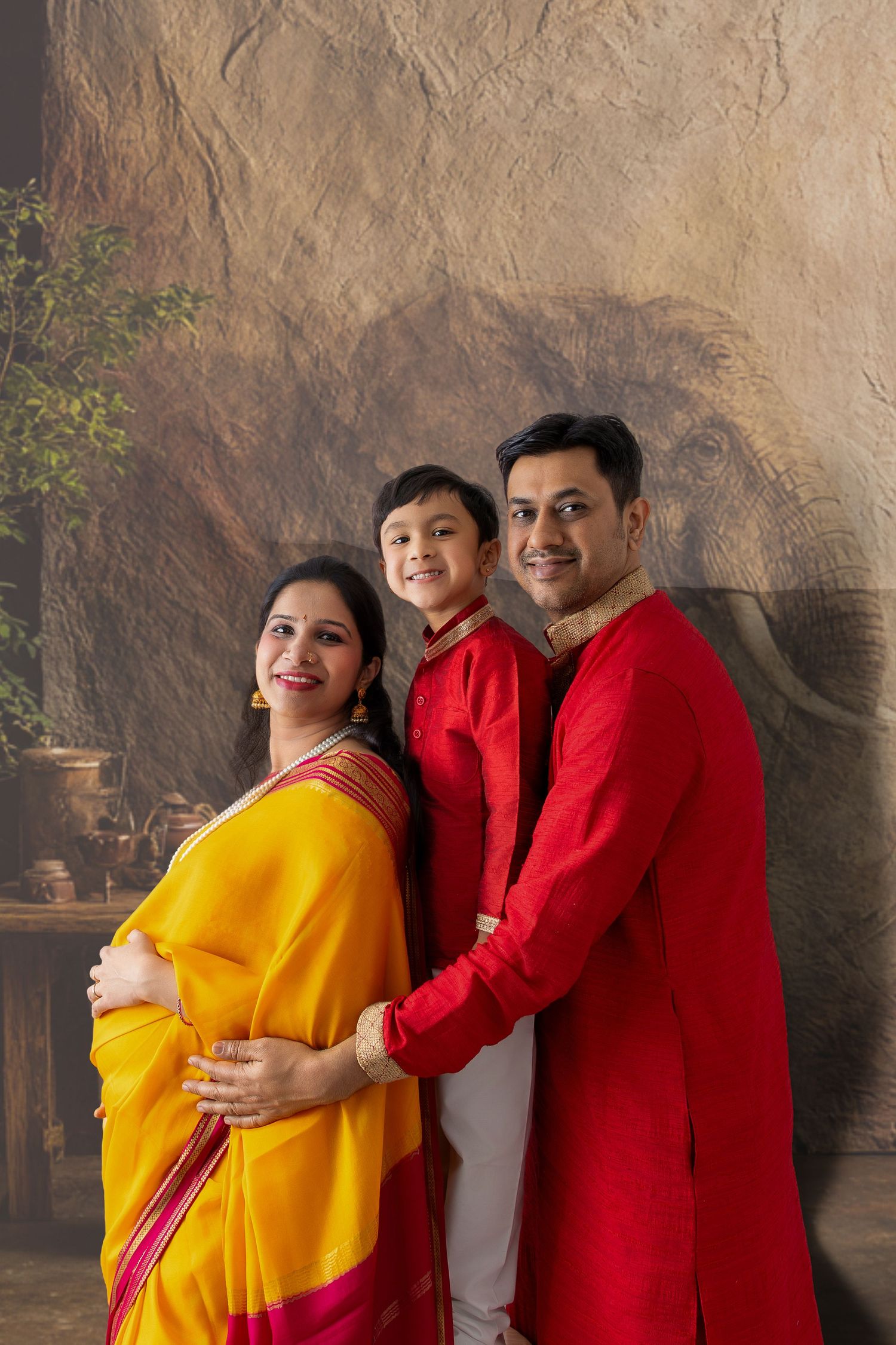 Indian family in traditional attire smiling together against elephant mural background.