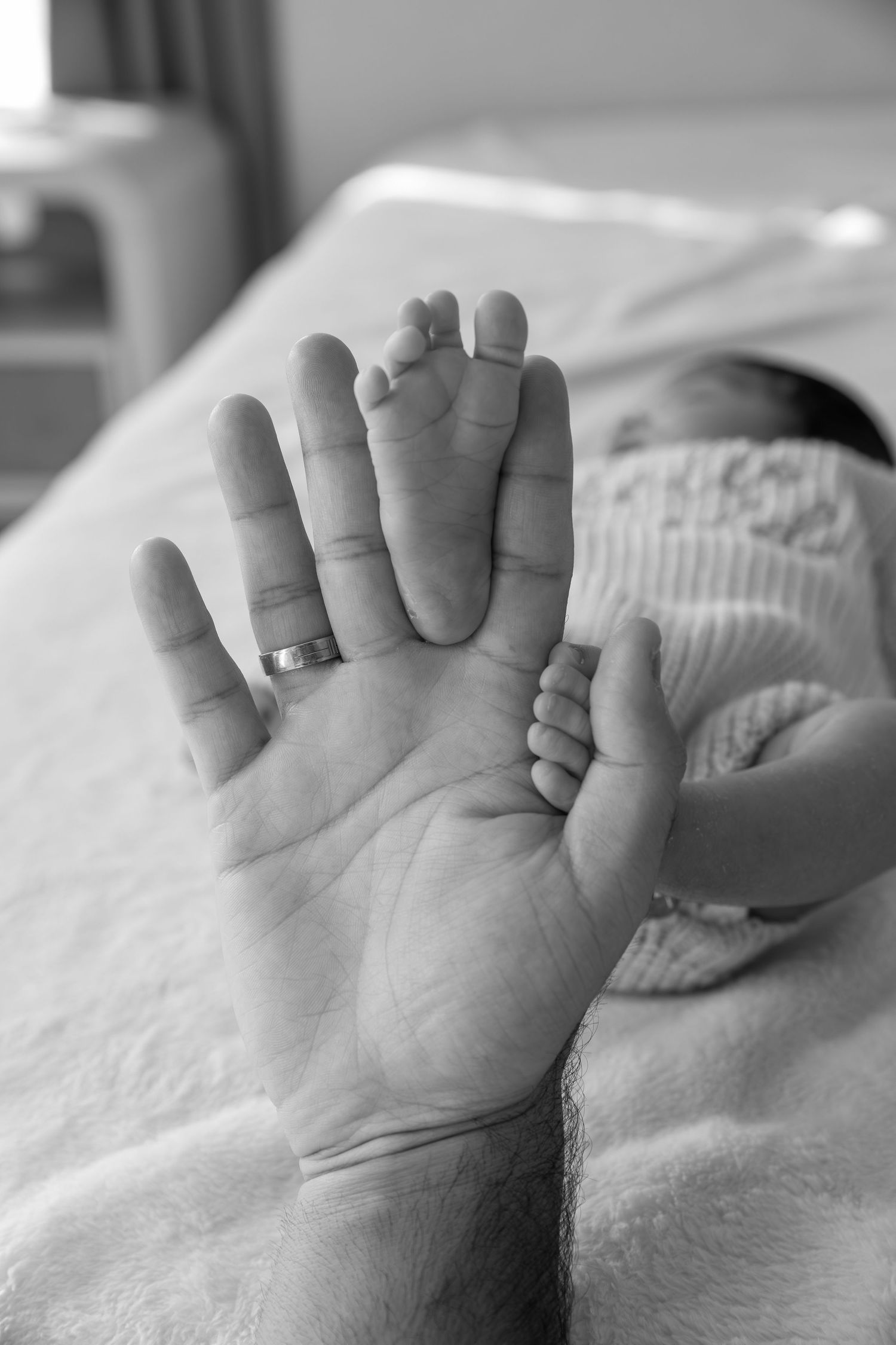 Black and white close-up images of tiny newborn baby feet and hands against white bedding.