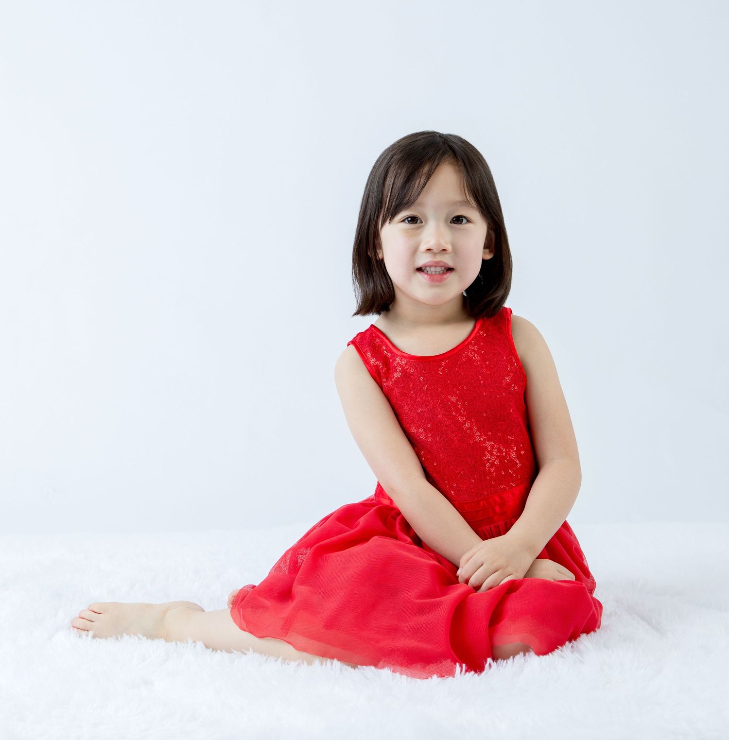 Playful pose in a festive red party dress against white studio backdrop.