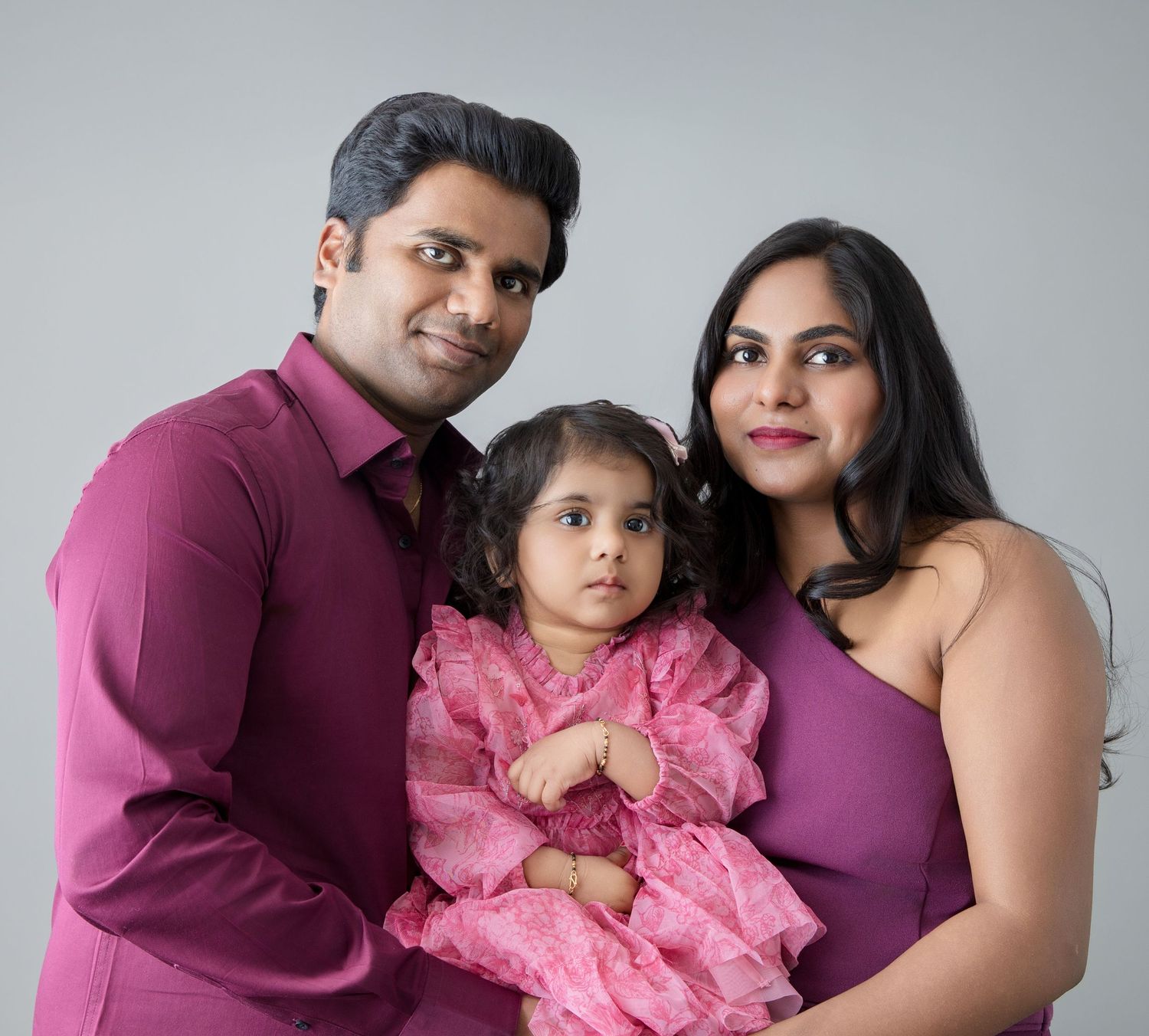 Studio portrait of a family in coordinated purple and pink outfits against a grey background.