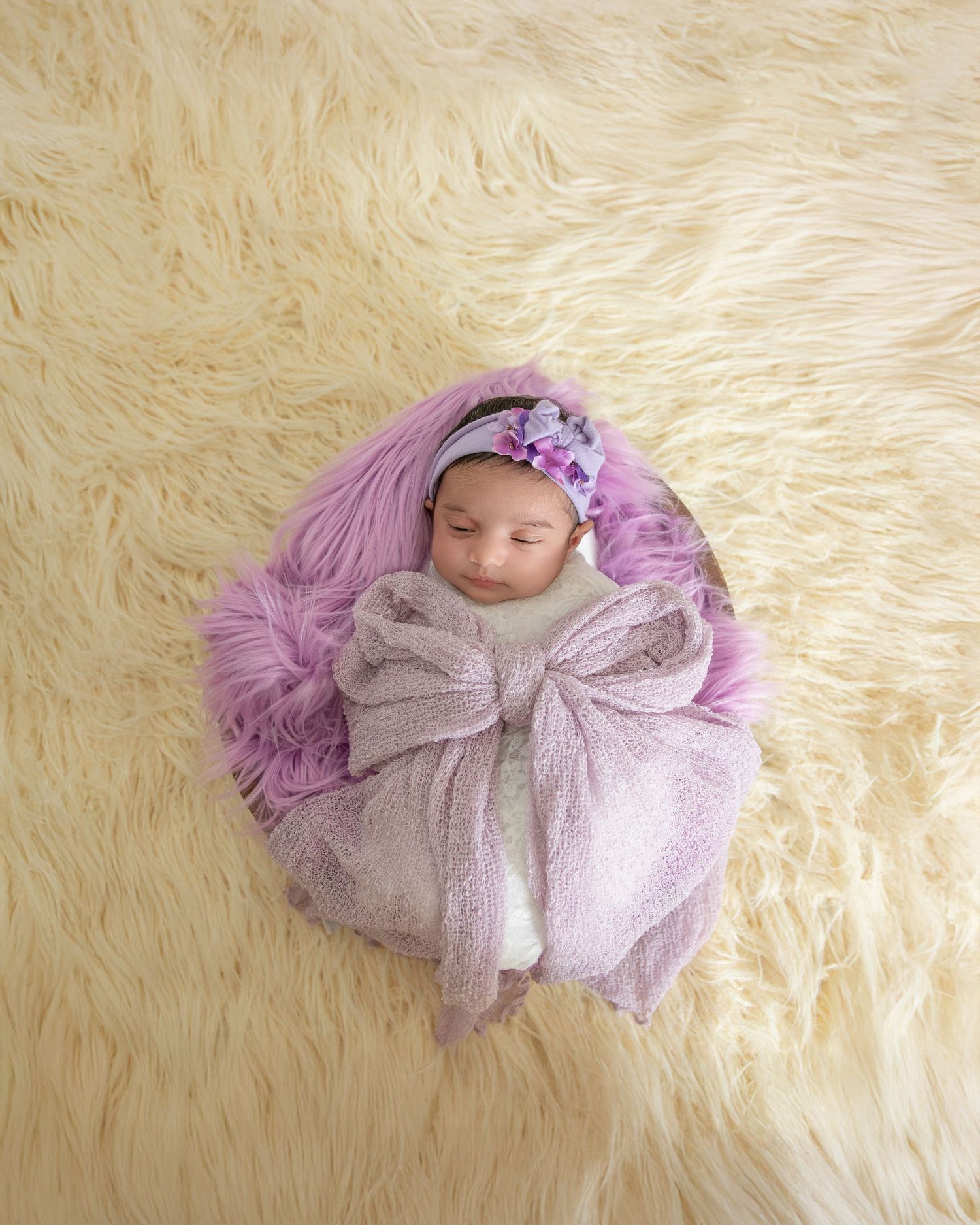 A sleeping newborn wrapped in a soft gray bow blanket lies on a cream-colored fluffy rug in a series of poses.