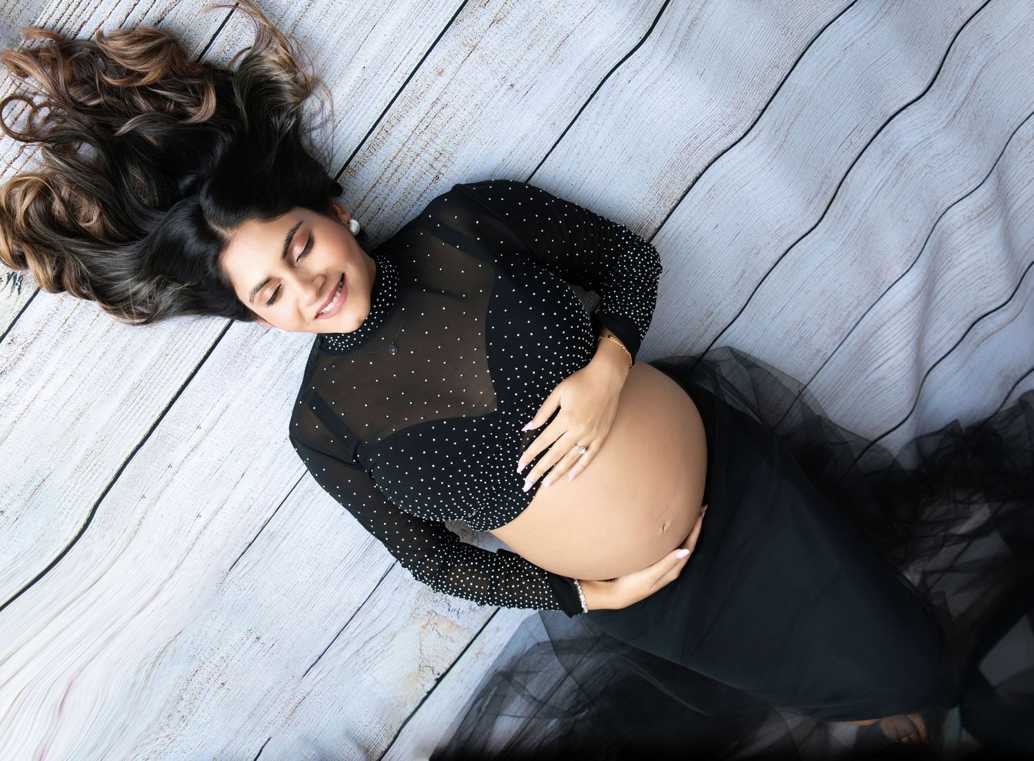 Maternity portrait series in black dress against rustic wooden floor background.