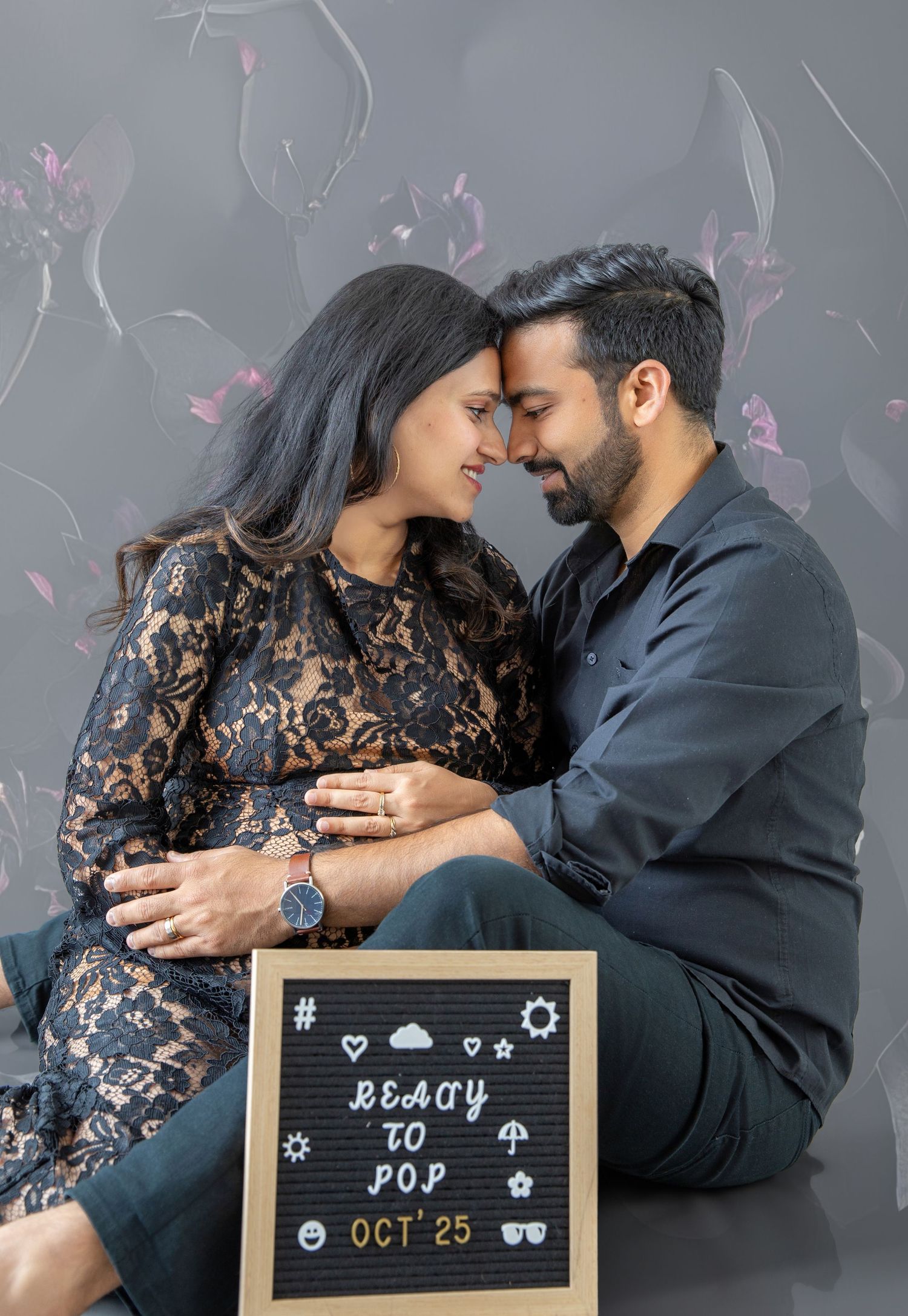 Couple sharing a tender maternity moment sitting together, holding baby bump, with a Ready to Pop Oct 25 sign.