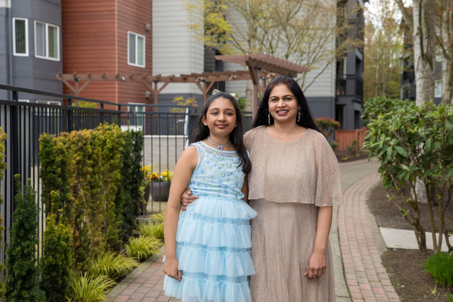 Two people walking together on a residential pathway with spring trees and townhouses.