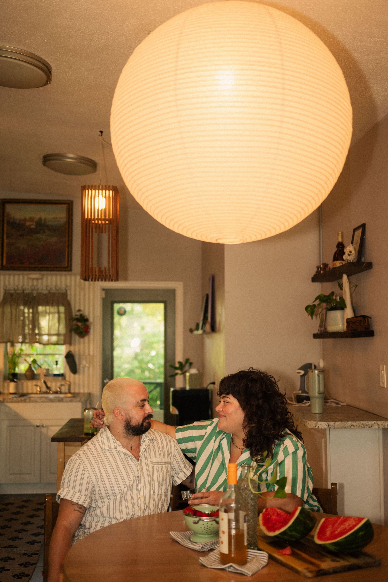 Kitchen dining scene under large paper lantern with watermelon slices on table.