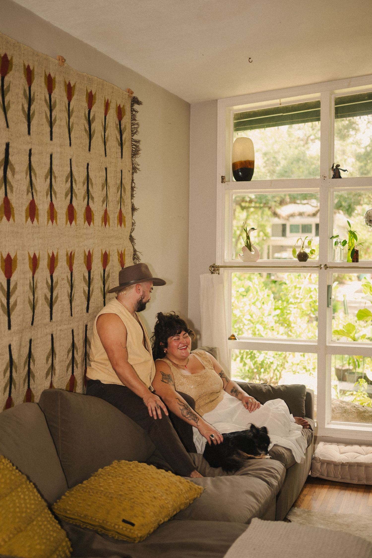 Couple relaxing on gray couch in room with decorative wall art and bright windows.
