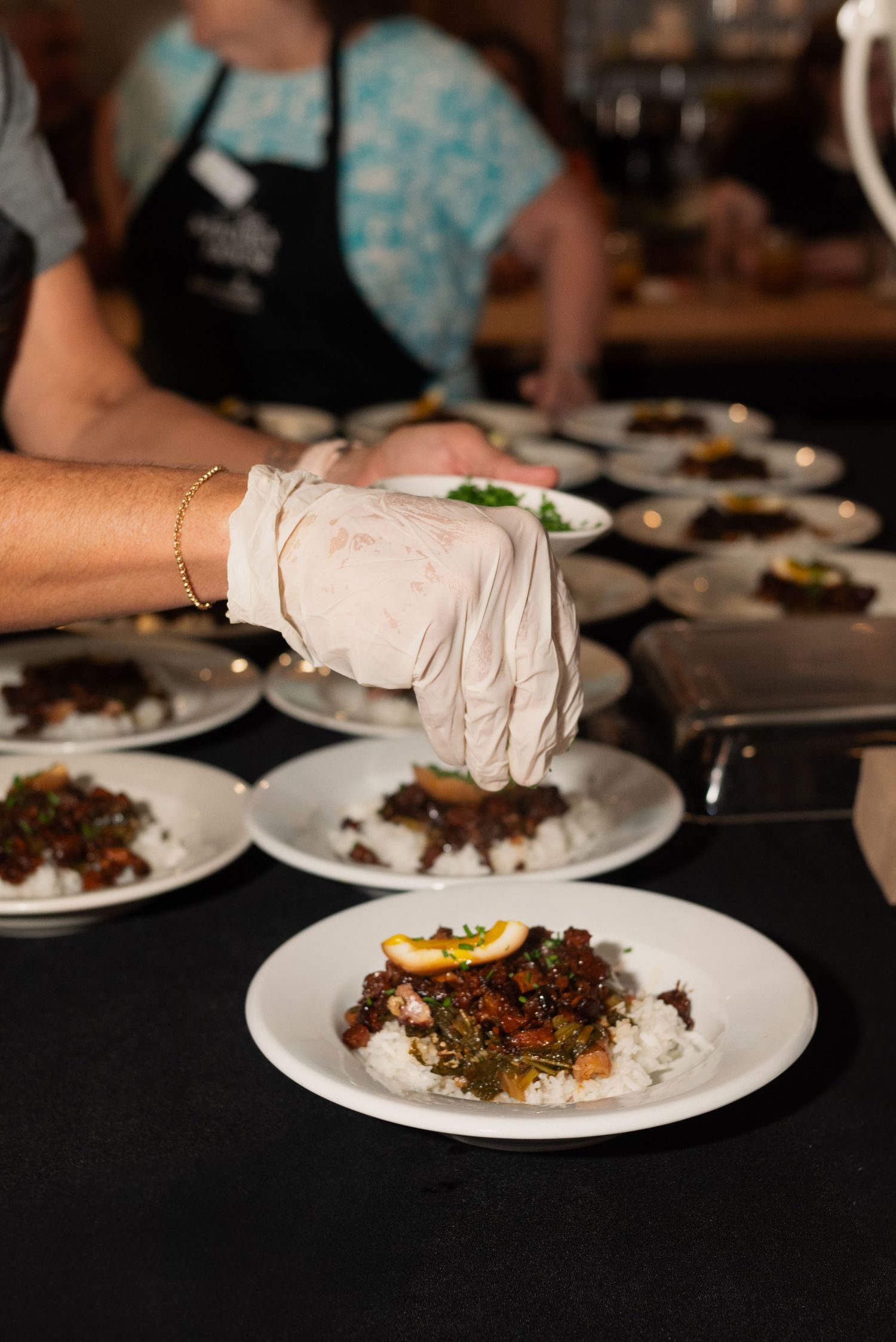 Gloved hands plating gourmet dishes on white plates in a restaurant kitchen.