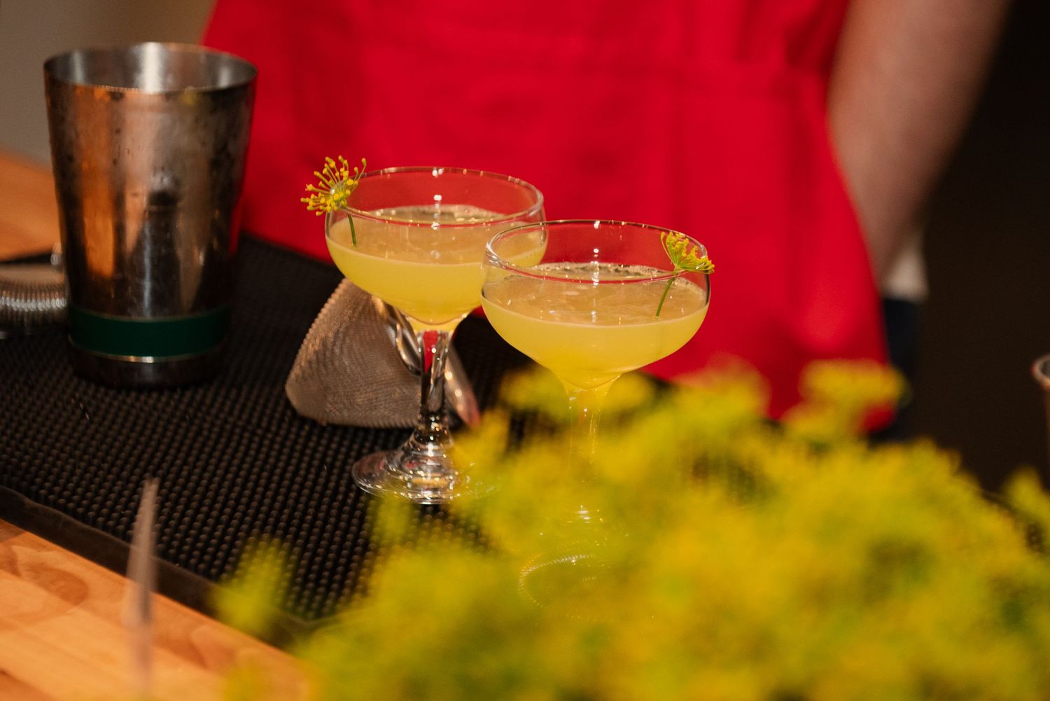 Colorful cocktails with garnishes are displayed on a bar counter with red and yellow accents.