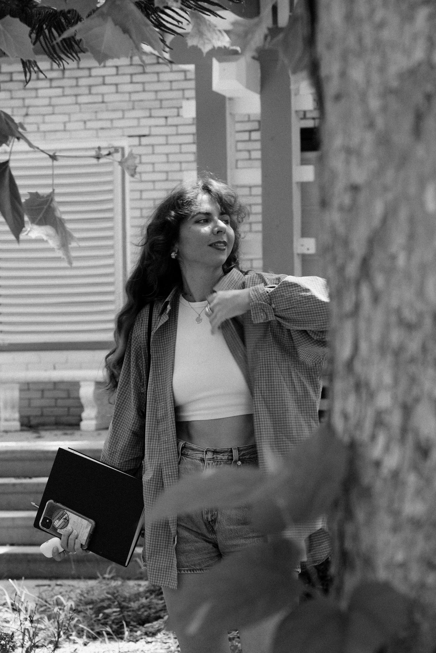 A figure in black and white poses artistically against a brick wall background.
