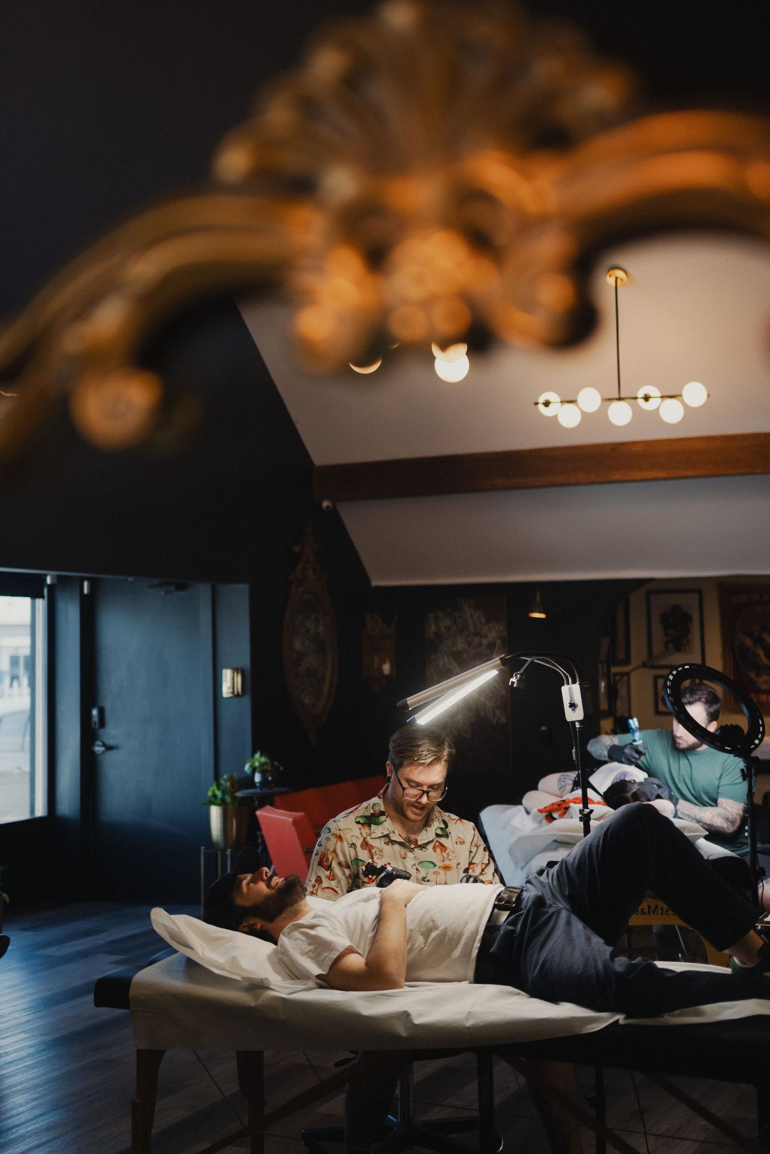 Tattoo session in progress in a dimly lit studio with modern ceiling lights.
