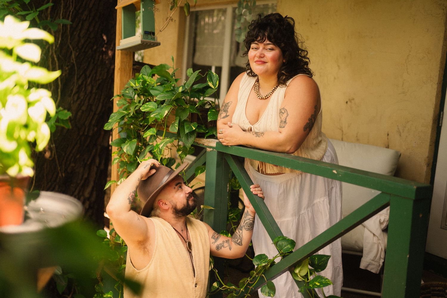 A couple embraces near a green railing with plants in the background.