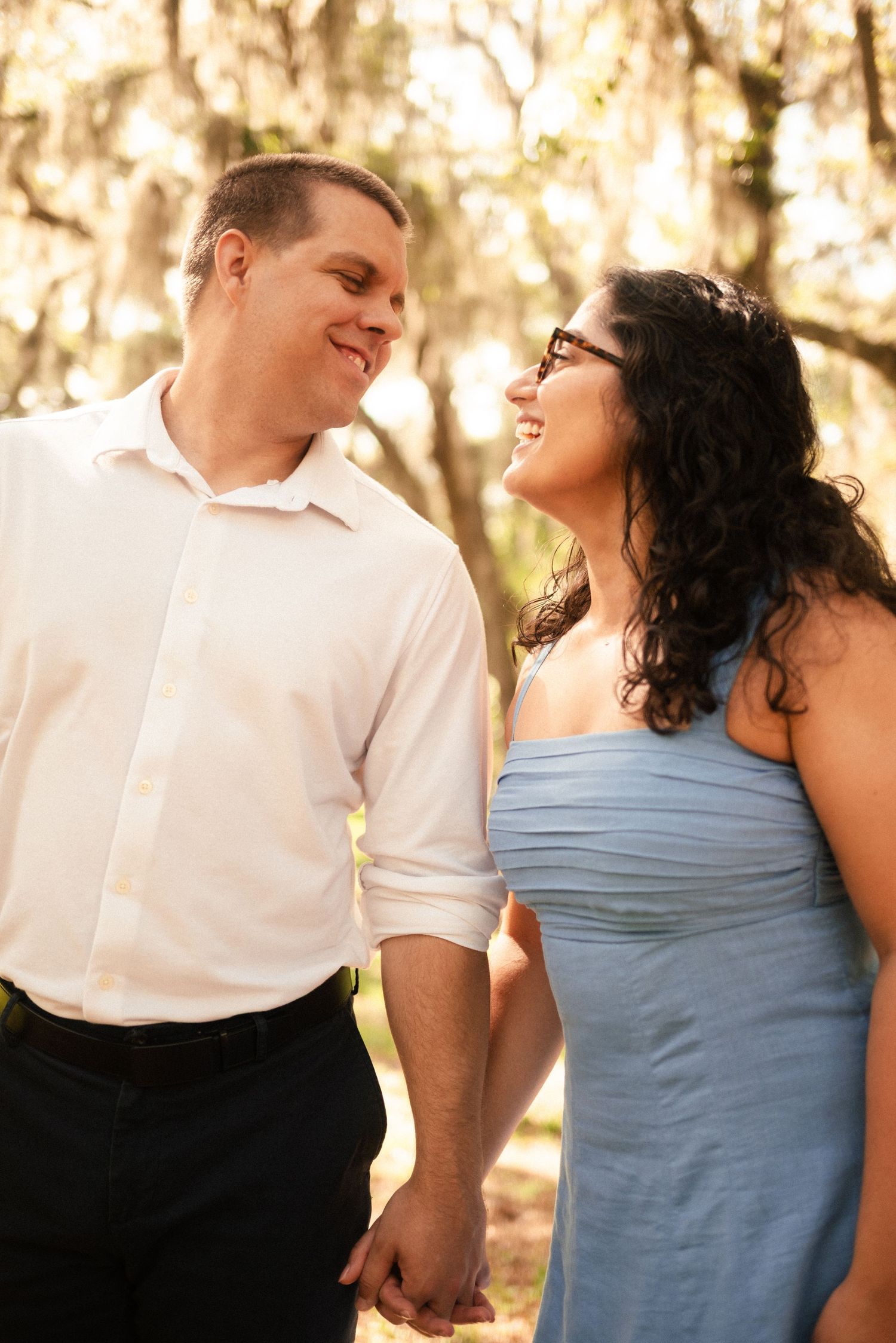 Romantic couple sharing joyful moments in golden afternoon light under Spanish moss trees.
