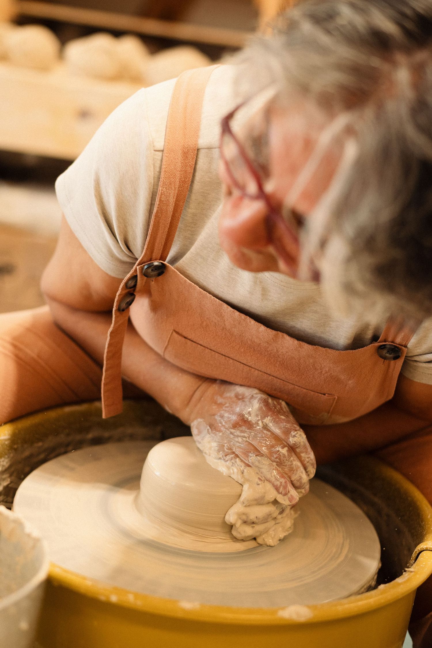 Artisan working on pottery wheel shaping clay with focused concentration.