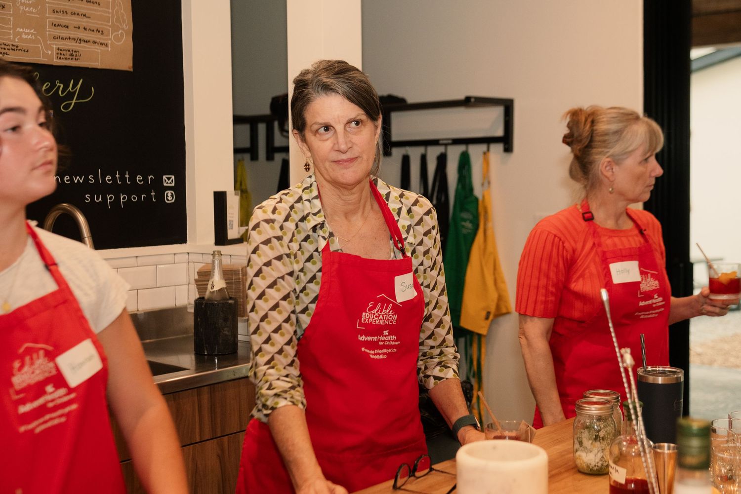 Participants in red aprons gathered around a counter during a cooking workshop.