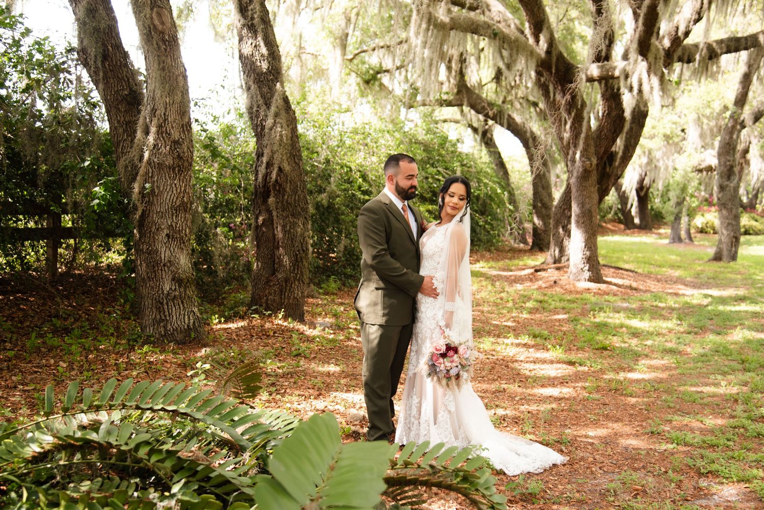 Newlyweds pose for photos under moss-draped oak trees in a scenic outdoor setting.
