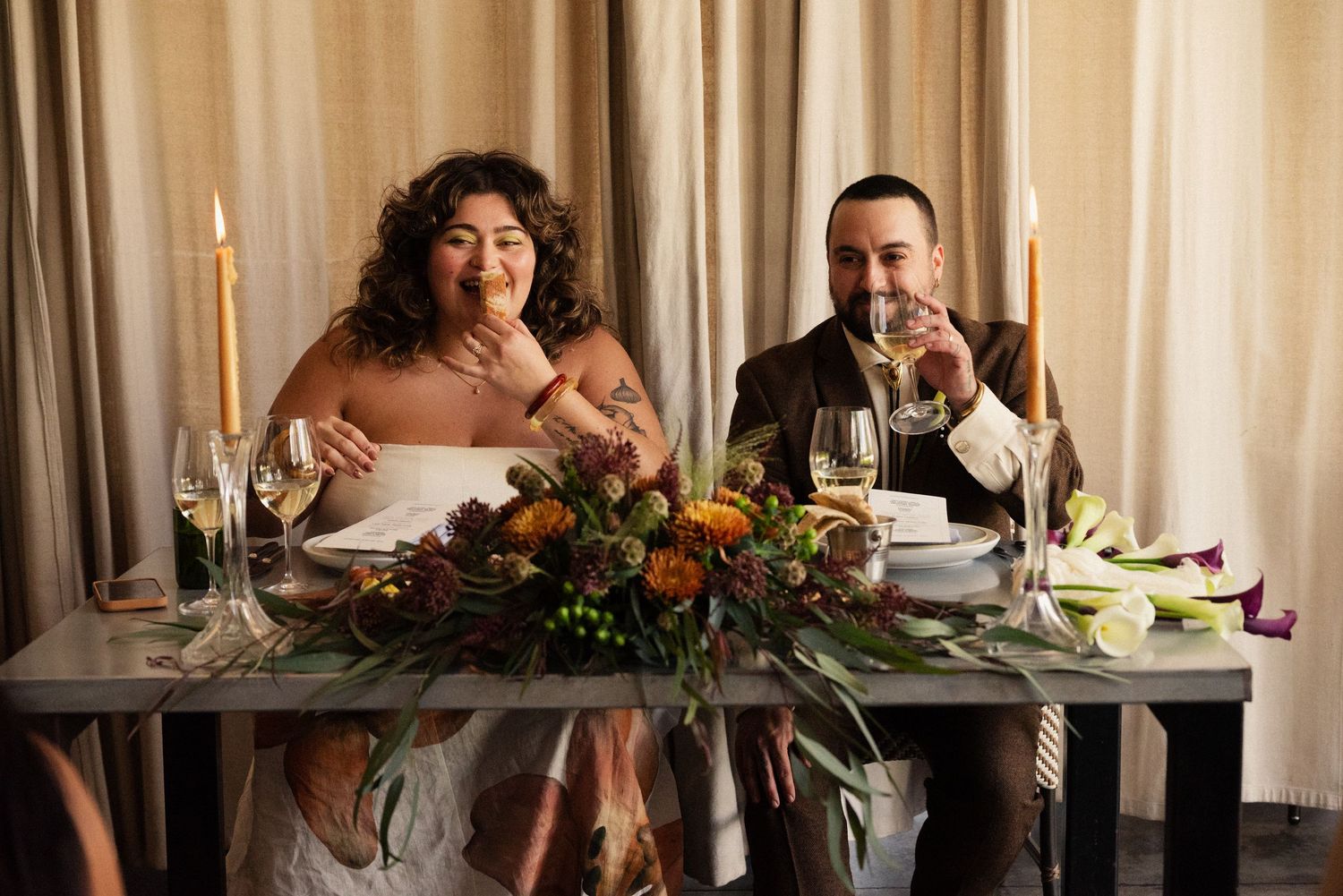 A couple shares a meal at a romantic table setting with wine and floral decorations.