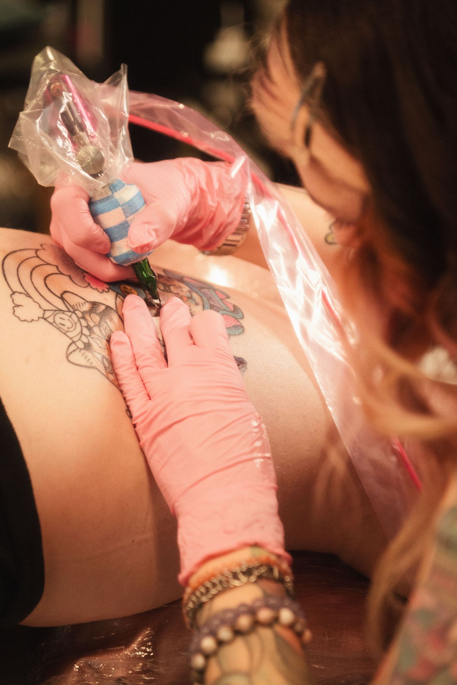 Close-up of a tattoo artist working on a detailed design with pink gloves and professional equipment.