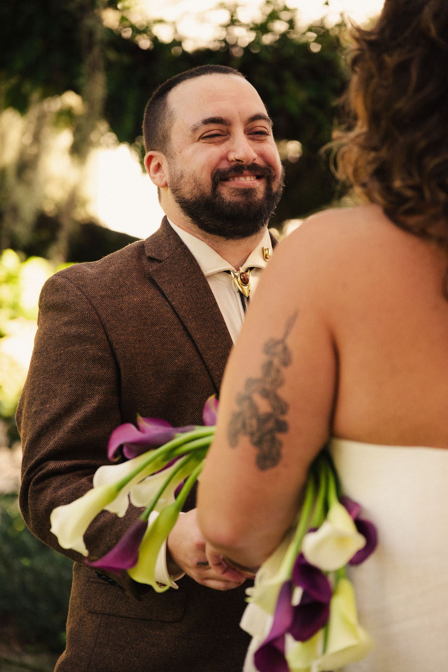 Wedding moment outdoors with brown suit and calla lily bouquet.
