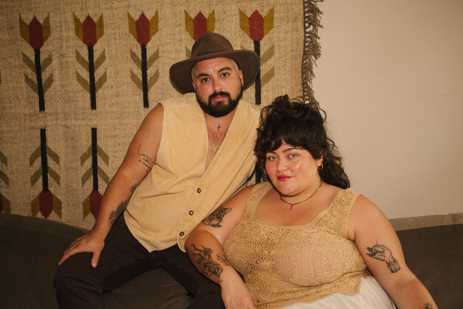 Two people in beige vintage clothing sitting together on dark furniture.