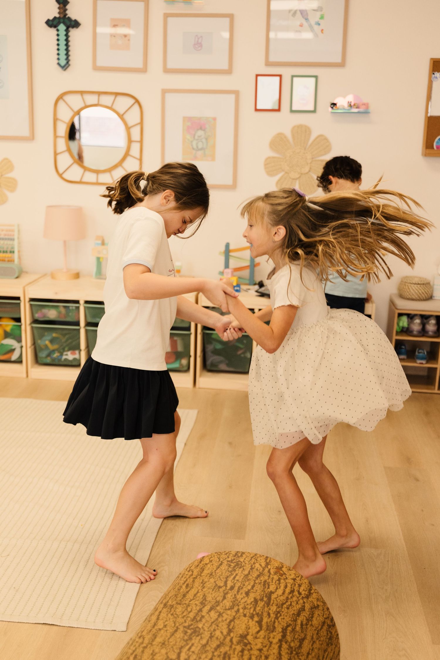 Two students dancing and playing together in a classroom with artwork on walls.