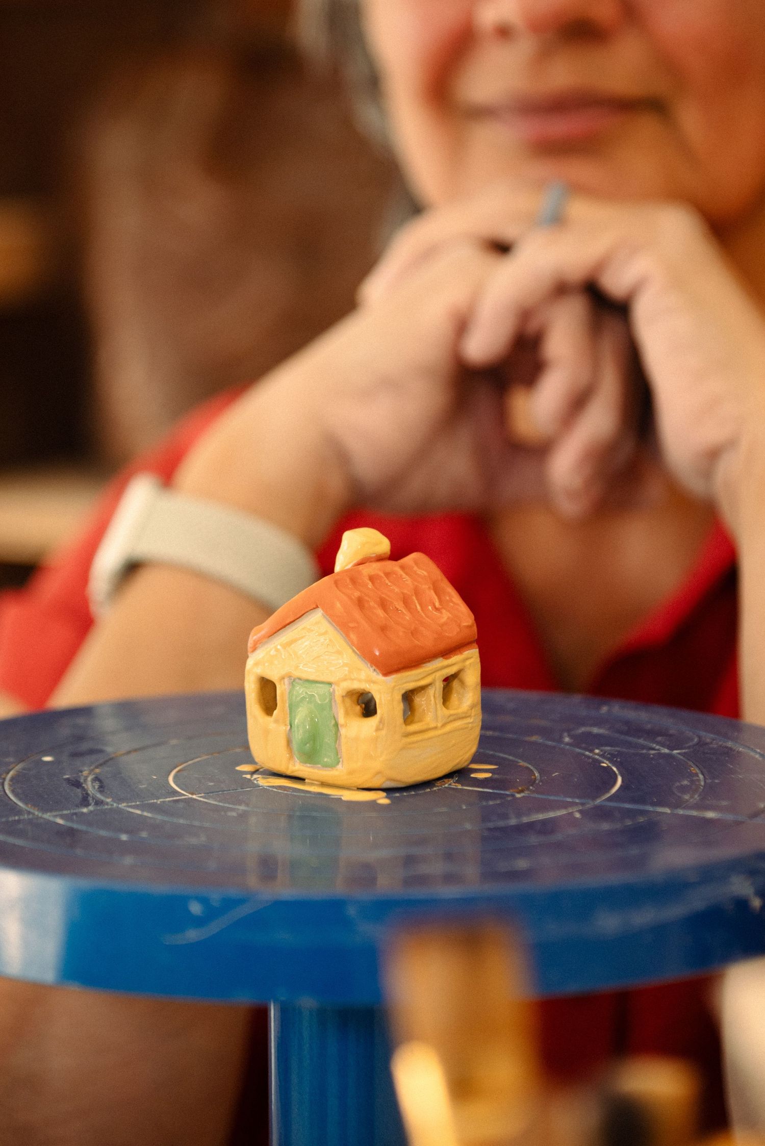 Miniature ceramic house displayed on a blue pottery wheel surface.