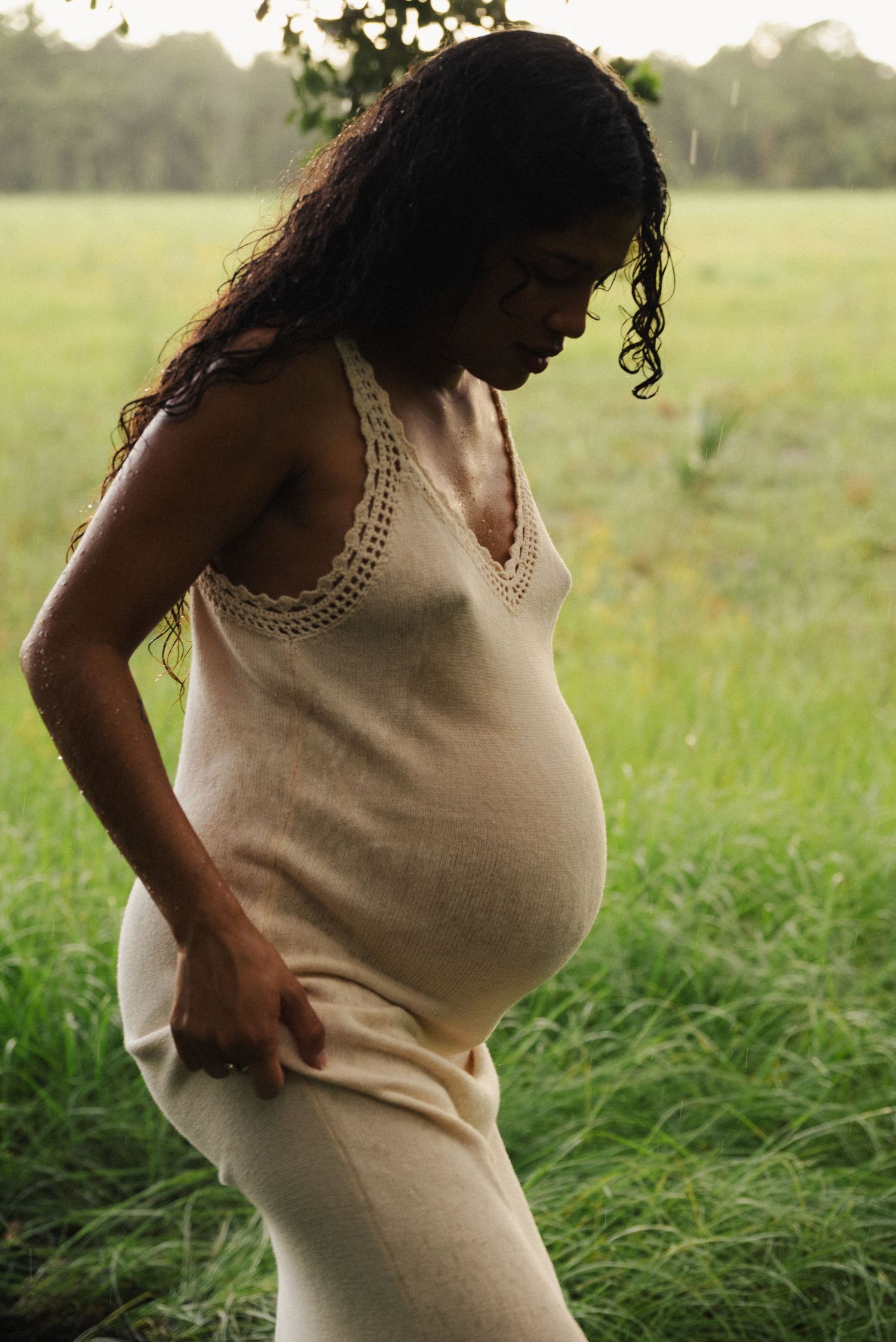 Person in cream-colored top standing in tall grass during golden hour.