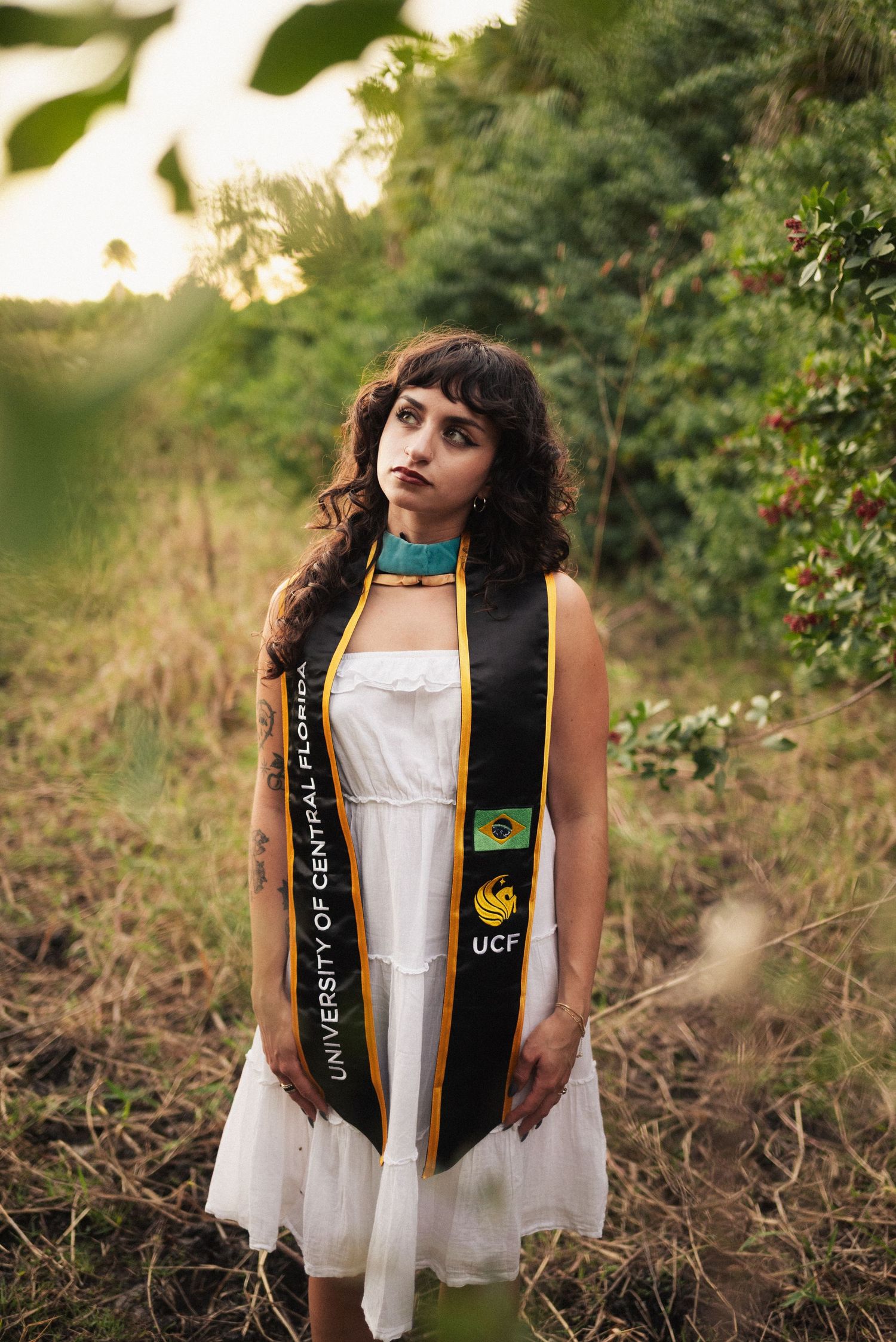 Graduate wearing UCF stole and white dress poses in outdoor setting.